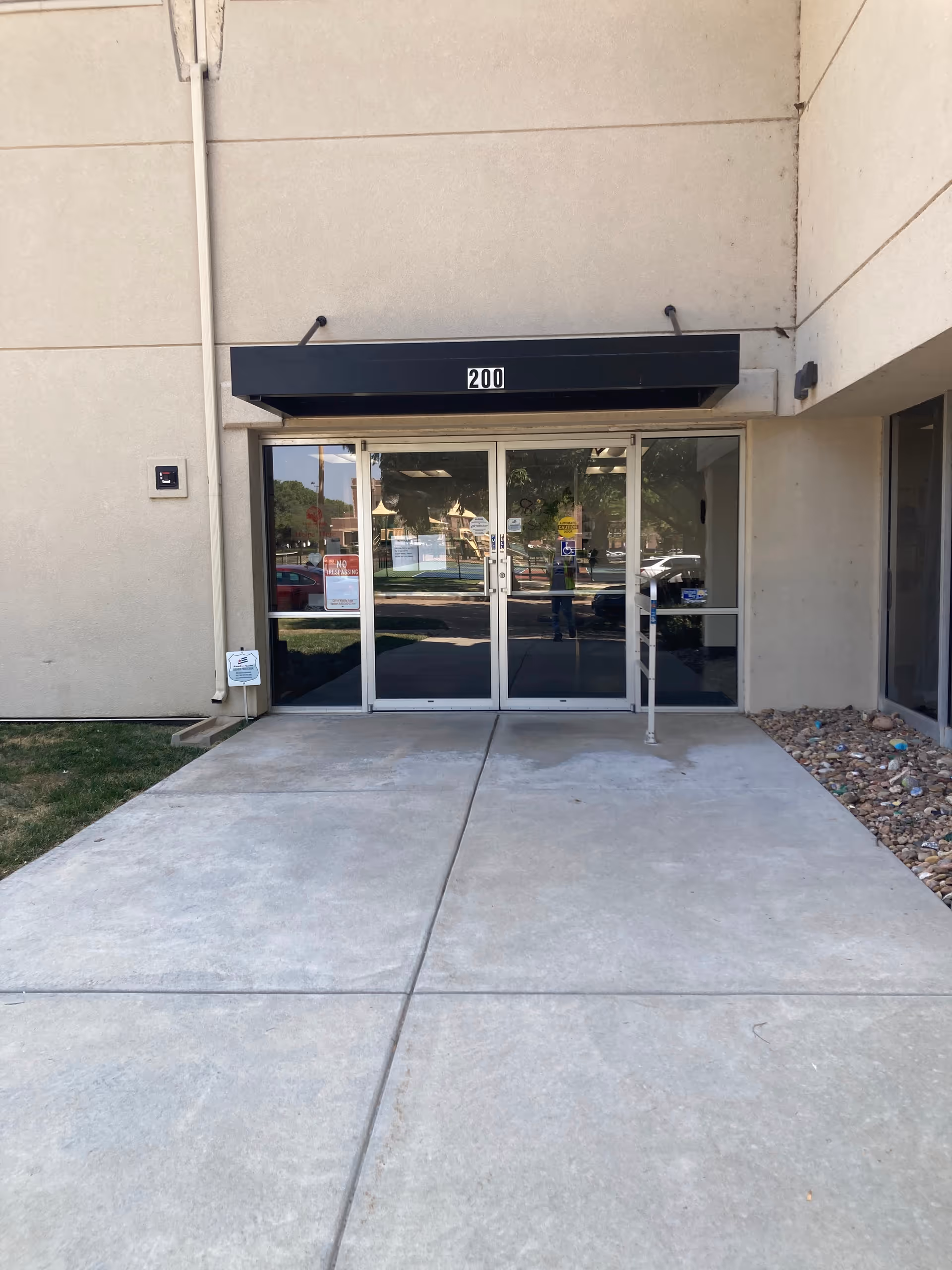 Glass double doors entrance to a beige building with a black awning reading 200