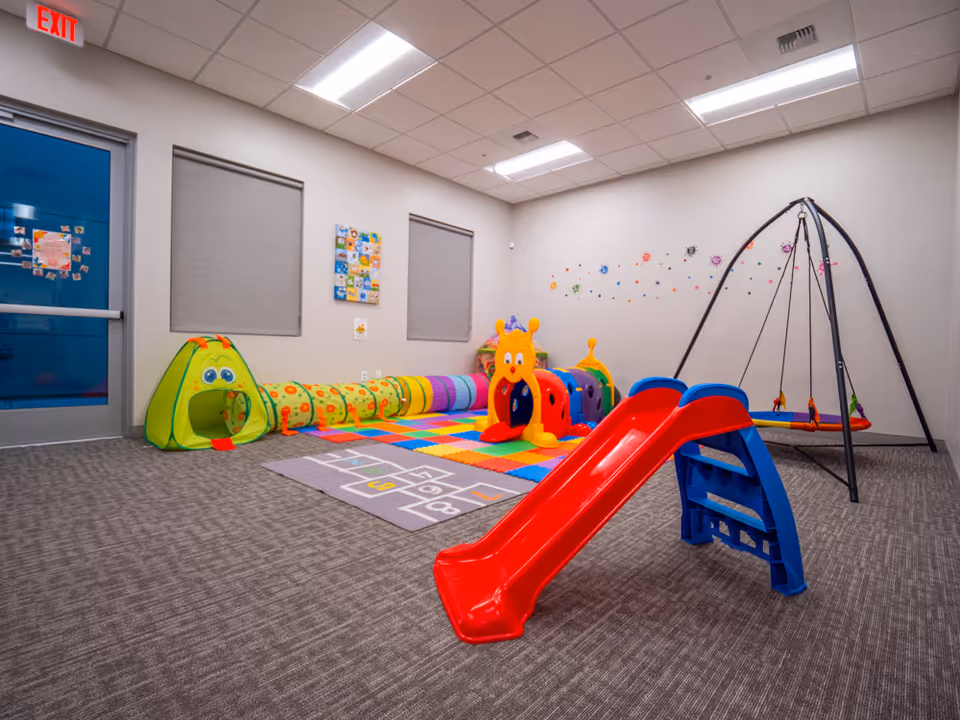 Colorful indoor therapy playroom with slide, tunnel, and soft mats.