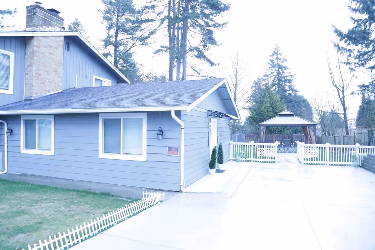 Blue, single-story facility exterior with a concrete driveway, white fence, and gazebo in yard.