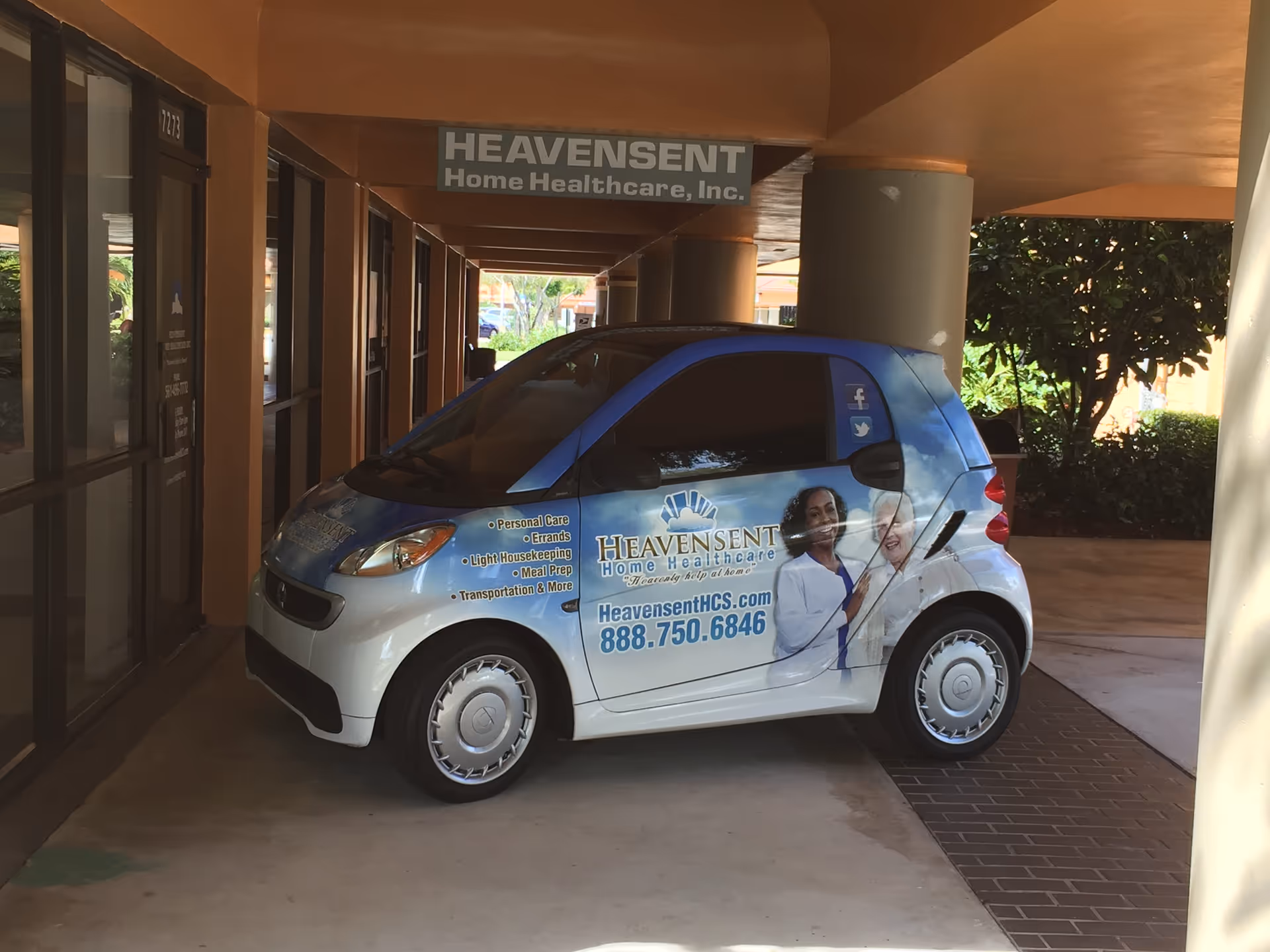 Blue and white Heavensent home healthcare van parked outside facility entrance under a covered walkway.