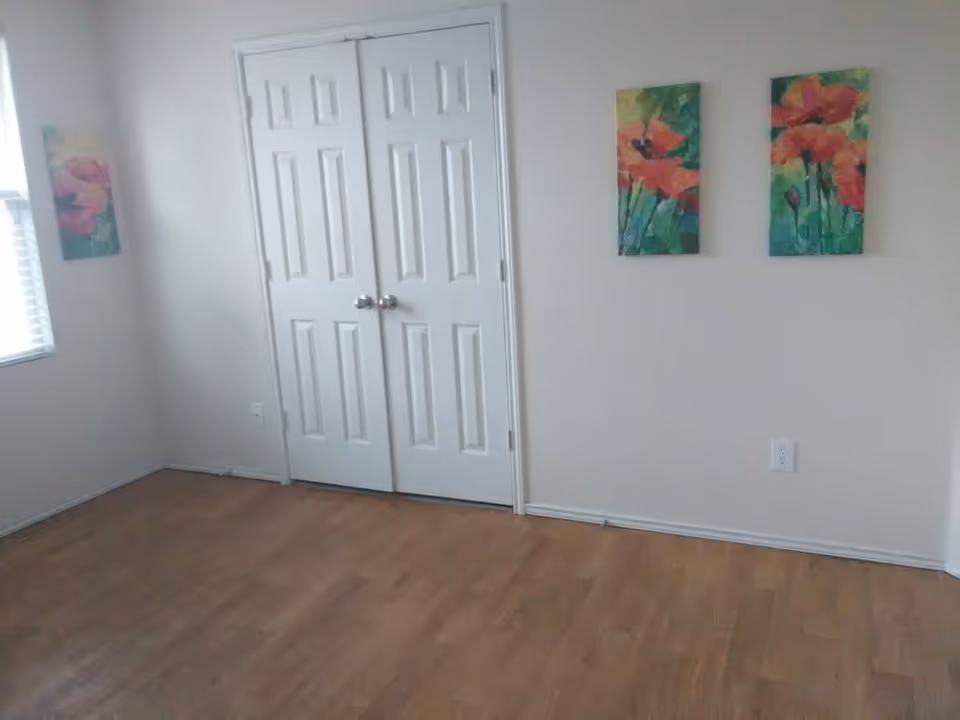 A small empty room with double closet doors, wall art, and a window.