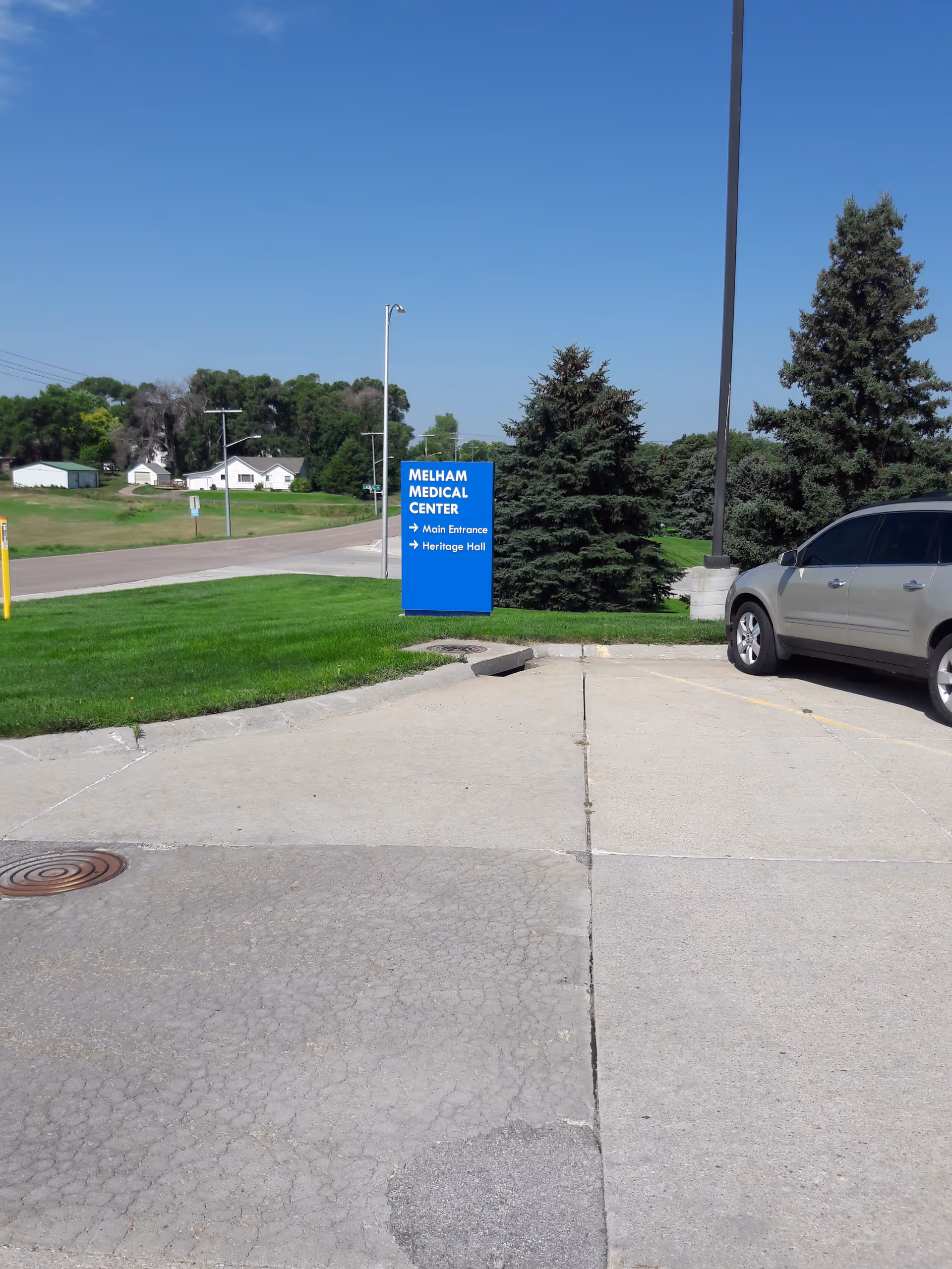 Blue Melham Medical Center sign near entrance with a gray SUV in the parking area.