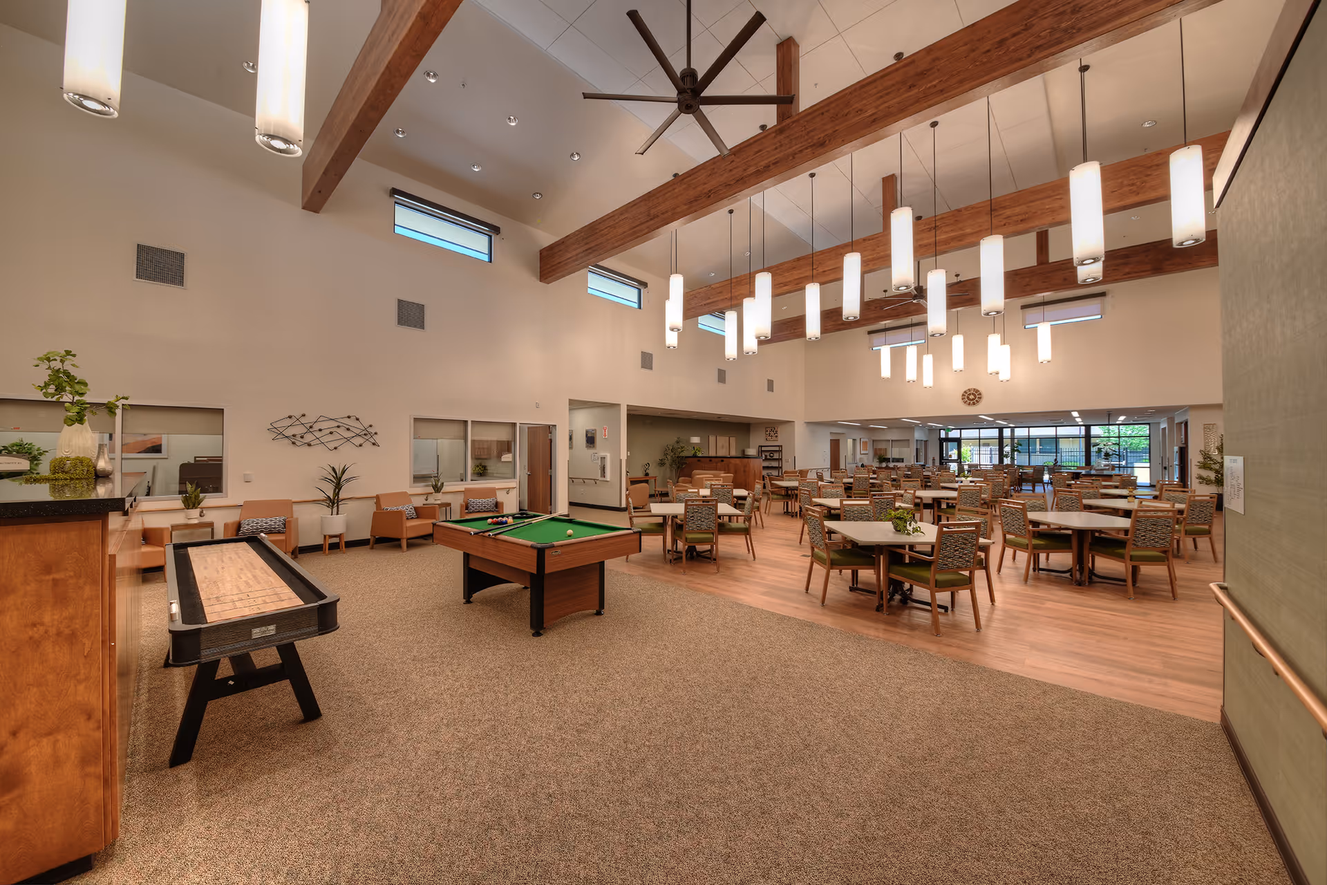 Spacious senior living common area with pool table, round dining tables, and lounge seating.