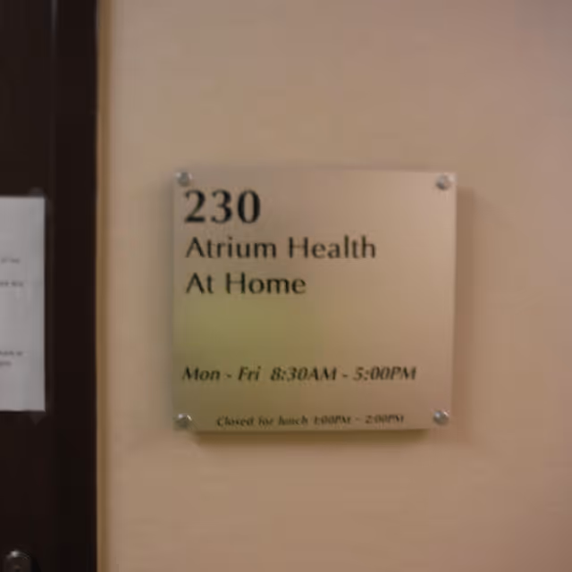 Wall plaque reading '230 Atrium Health At Home' with operating hours.