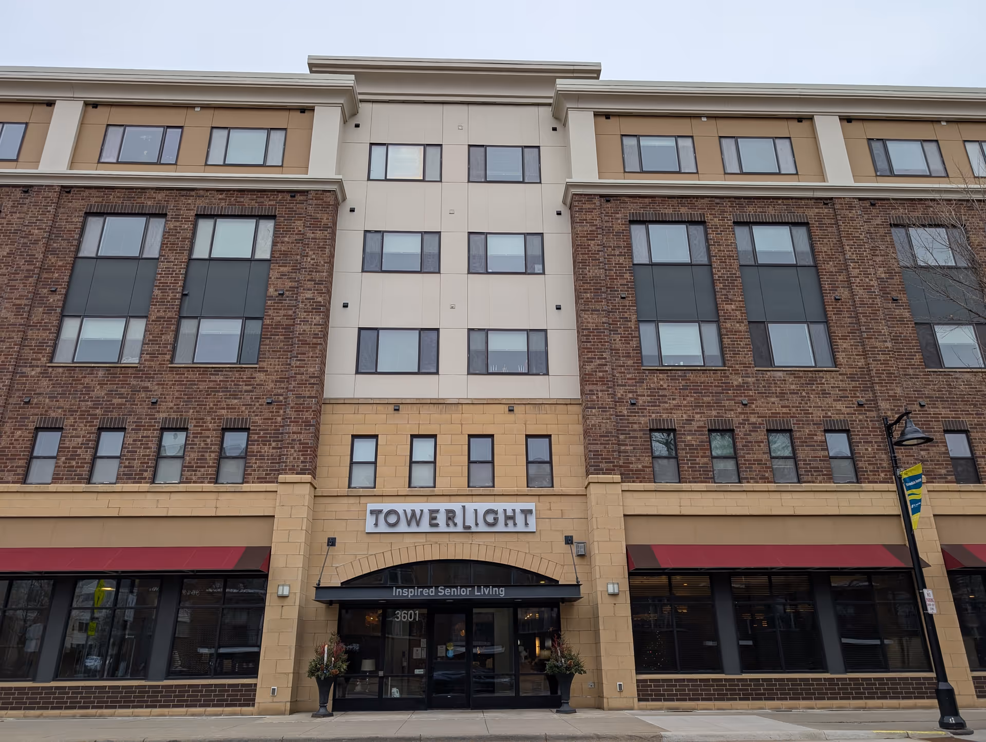 Front exterior of a multi-story brick and tan senior living building with a 'TOWERLIGHT' sign above the main entrance.