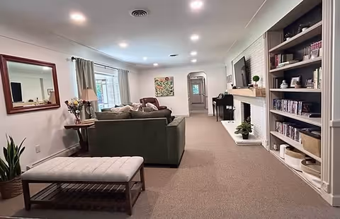 Bright senior living room featuring sofa, chairs, fireplace, and built-in bookshelves.