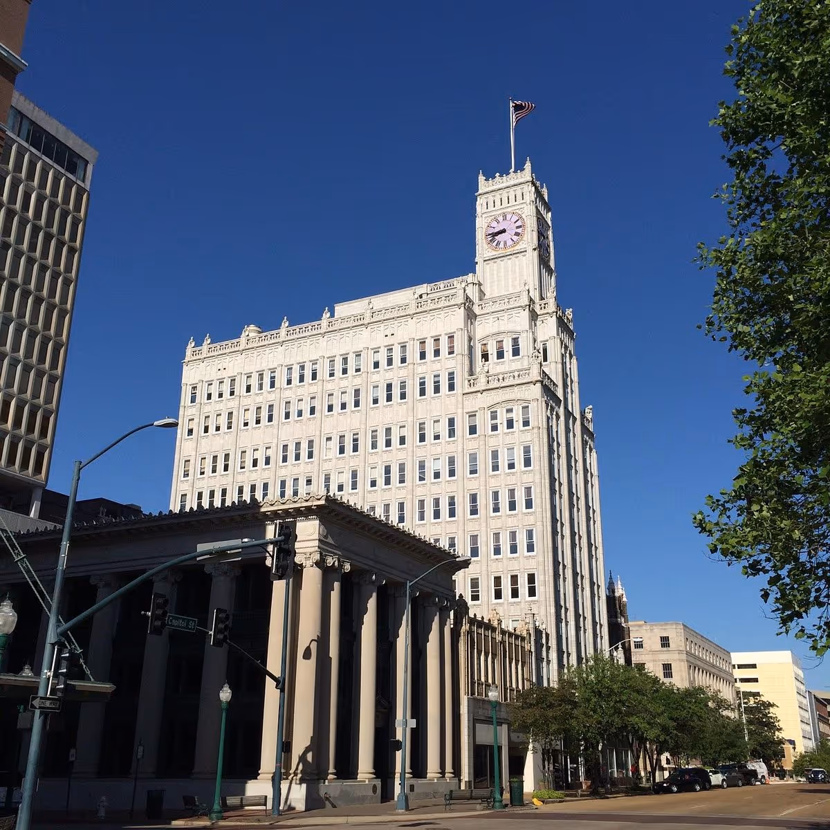 Tall historic clock-tower building on a city street under a blue sky.