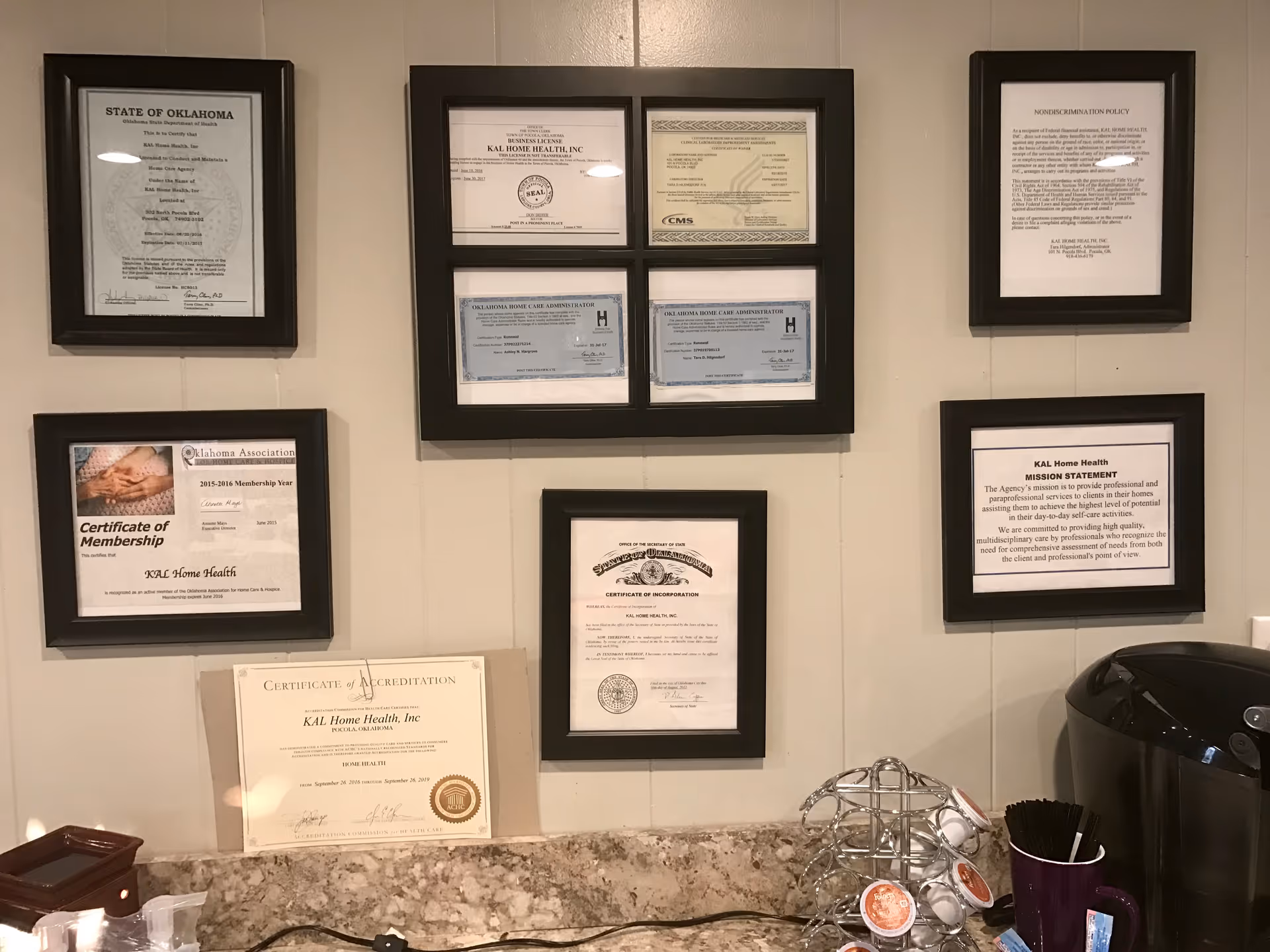 Wall of framed certificates and a coffee station in a KAL Home Health office.