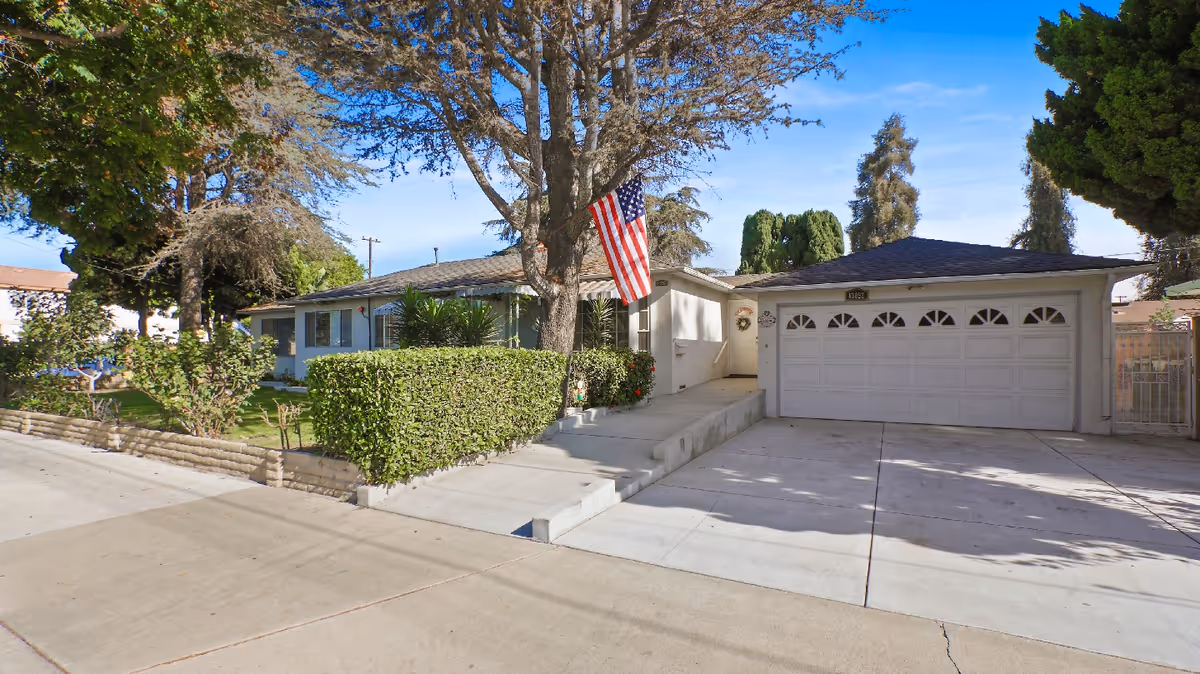 Sunny front exterior of a single-story senior living home with a two-car garage and flag.