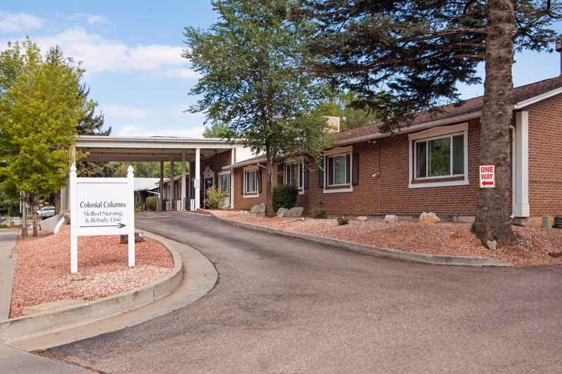 Exterior view of Colonial Columns facility with brick building, driveway, and sign.