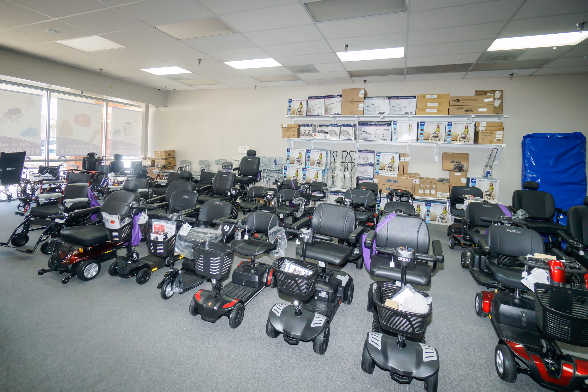 Indoor room filled with numerous mobility scooters lined up beside shelves of boxed gear