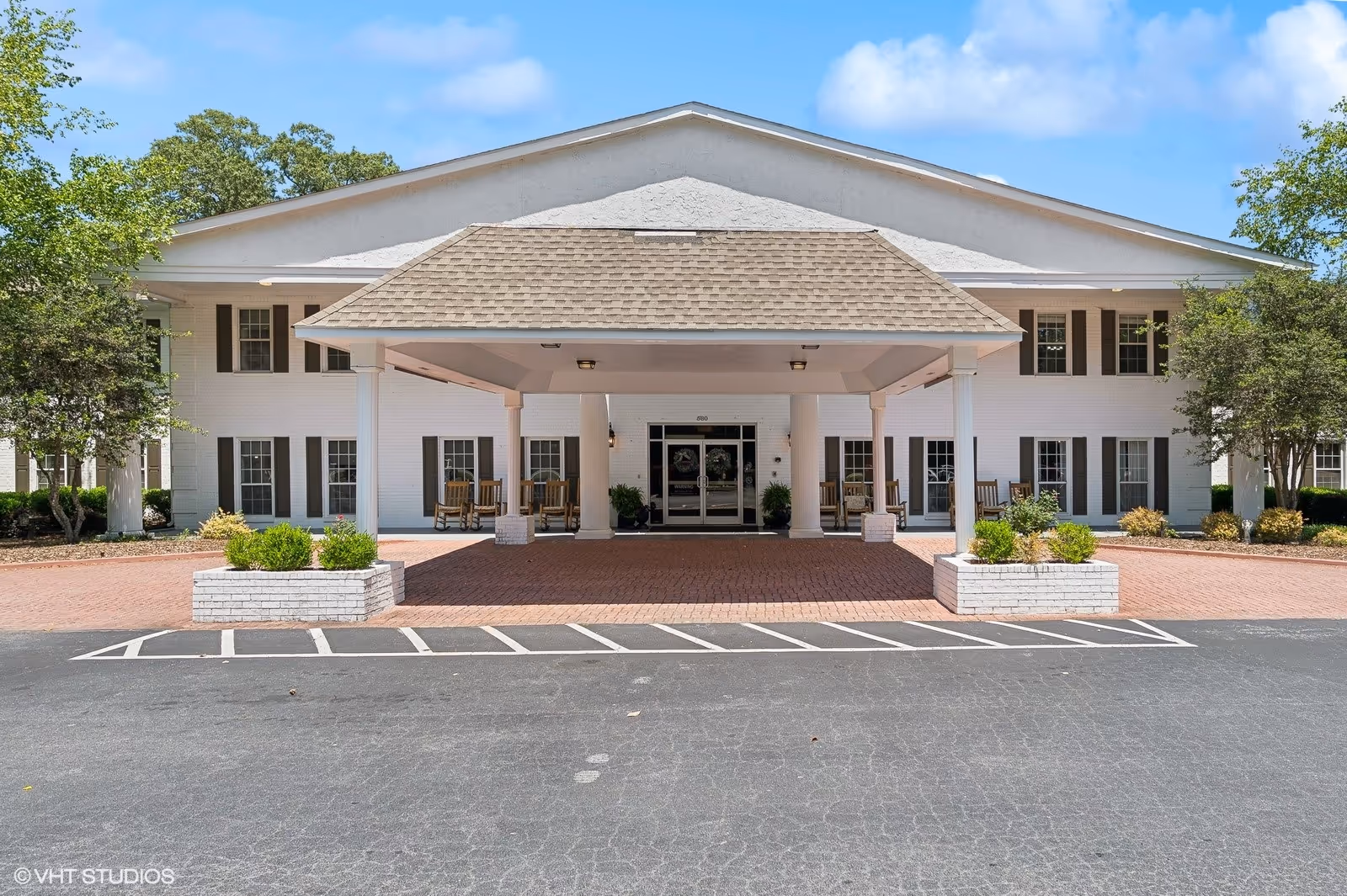 White brick senior living facility with a wide covered entry and brick driveway.