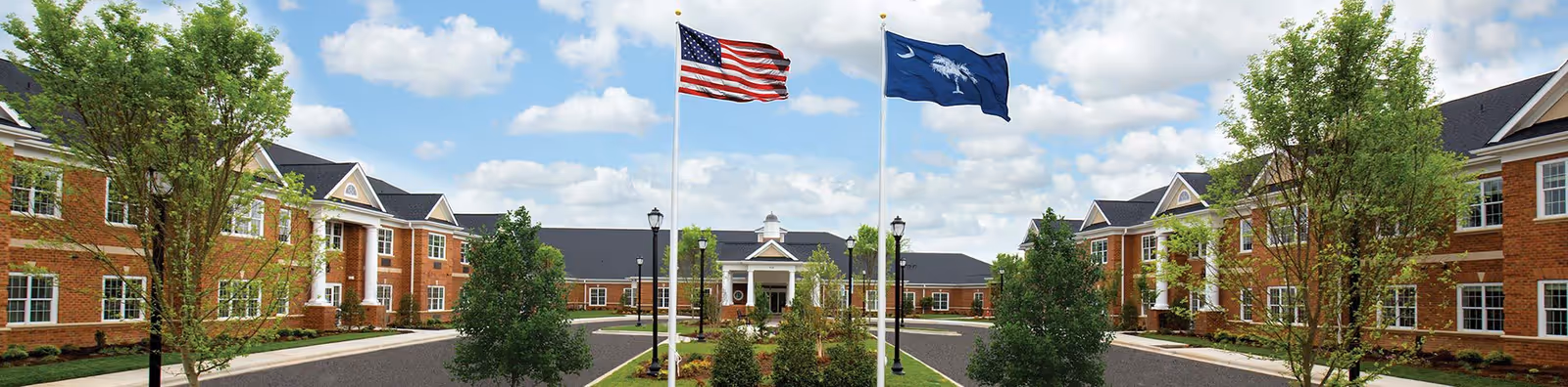 Symmetrical senior living campus with brick buildings, flagpoles, trees, and a central walkway.