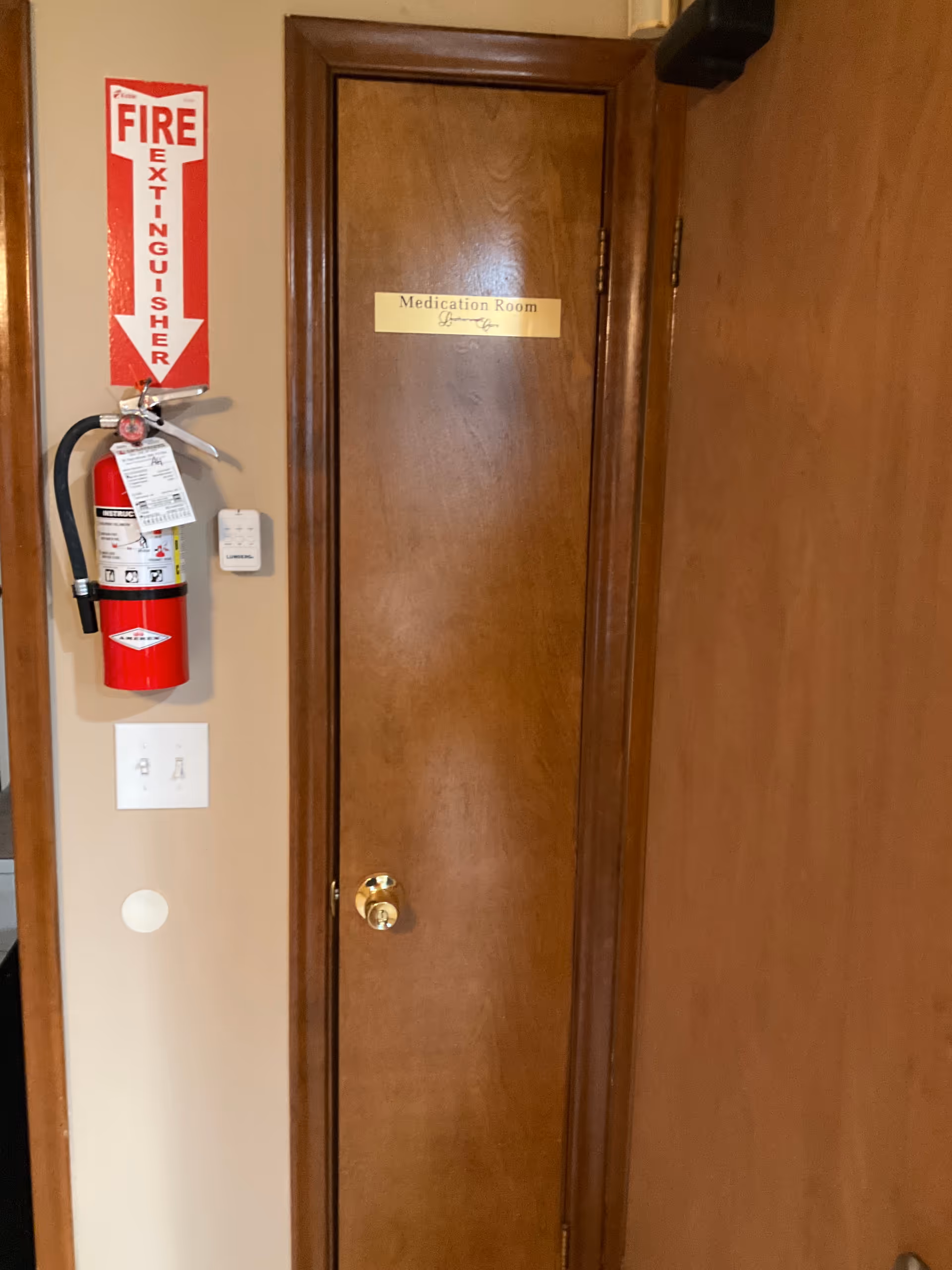Interior hallway with a wooden door labeled Medication Room and a fire extinguisher nearby.