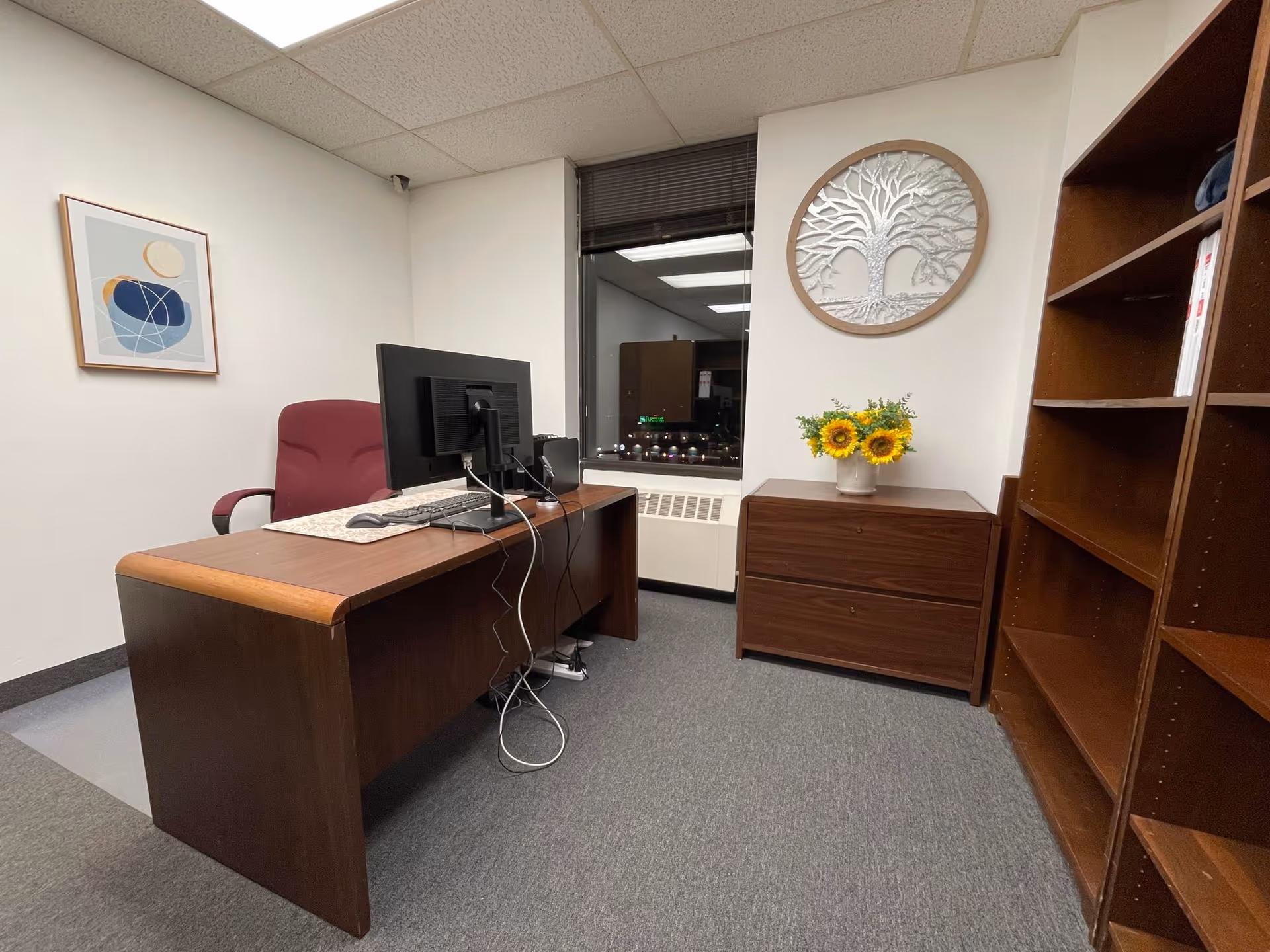 Office reception area with desk, computer, sunflower bouquet, and wooden shelves.