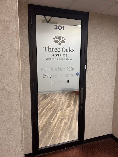 Glass entry door showing Three Oaks Hospice signage and an interior hallway beyond.