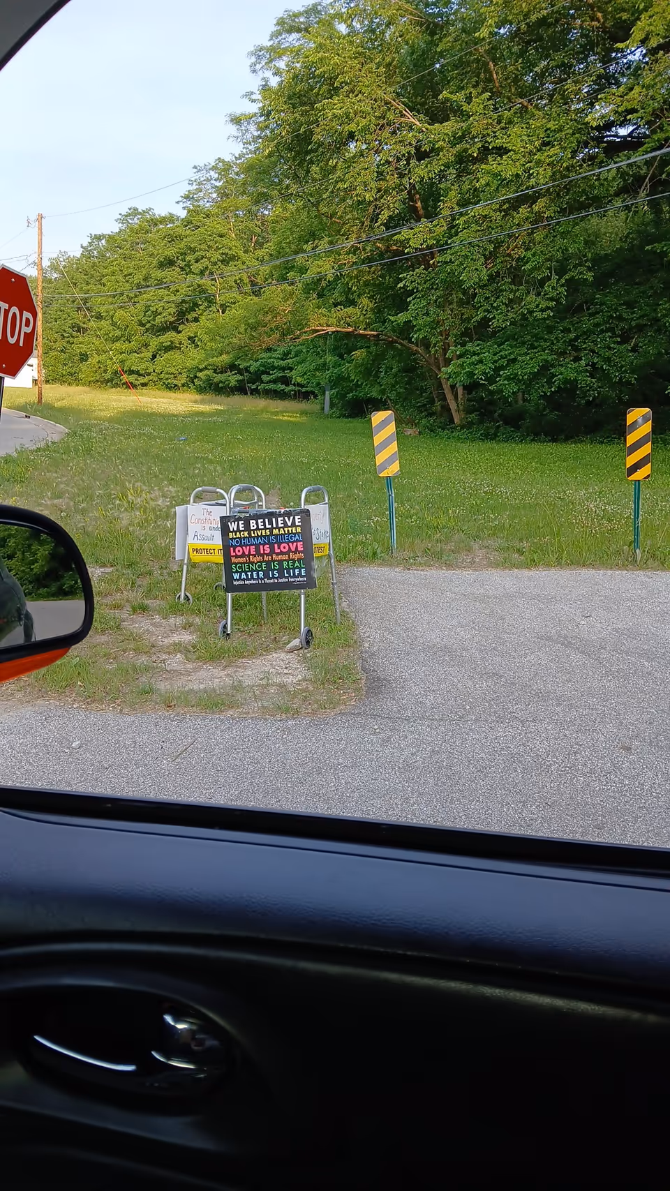 View from a car window of a grassy roadside with stop sign and colorful informational signs.