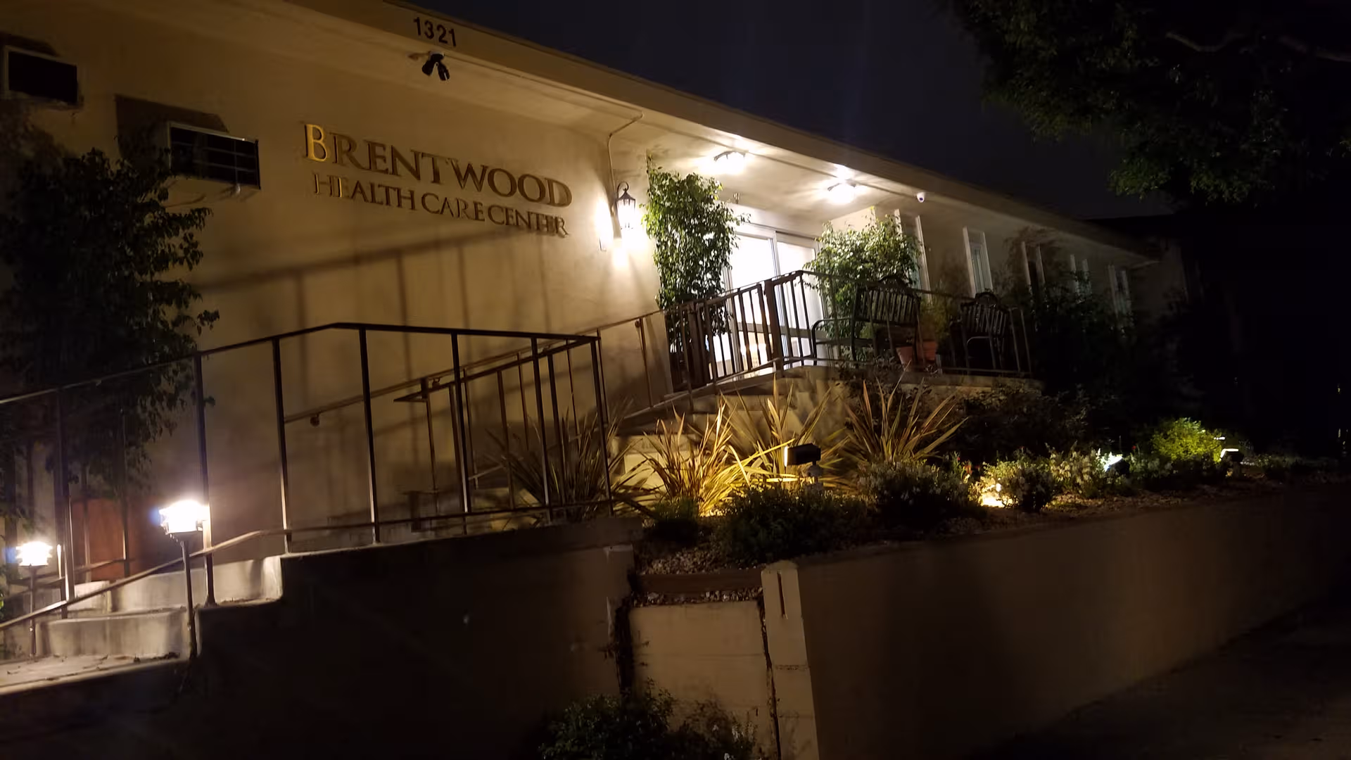 Night exterior of Brentwood Health Care Center with lit entrance and landscaped walkway.