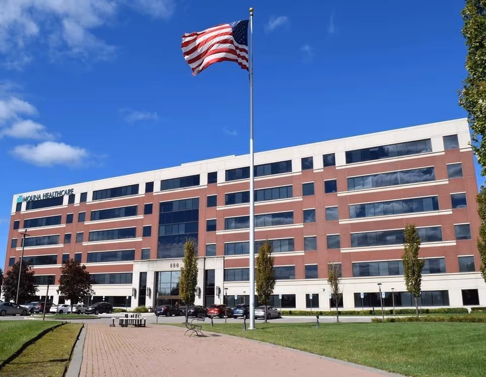Wide exterior view of a brick, multi-story healthcare building with a tall flagpole and lawn.