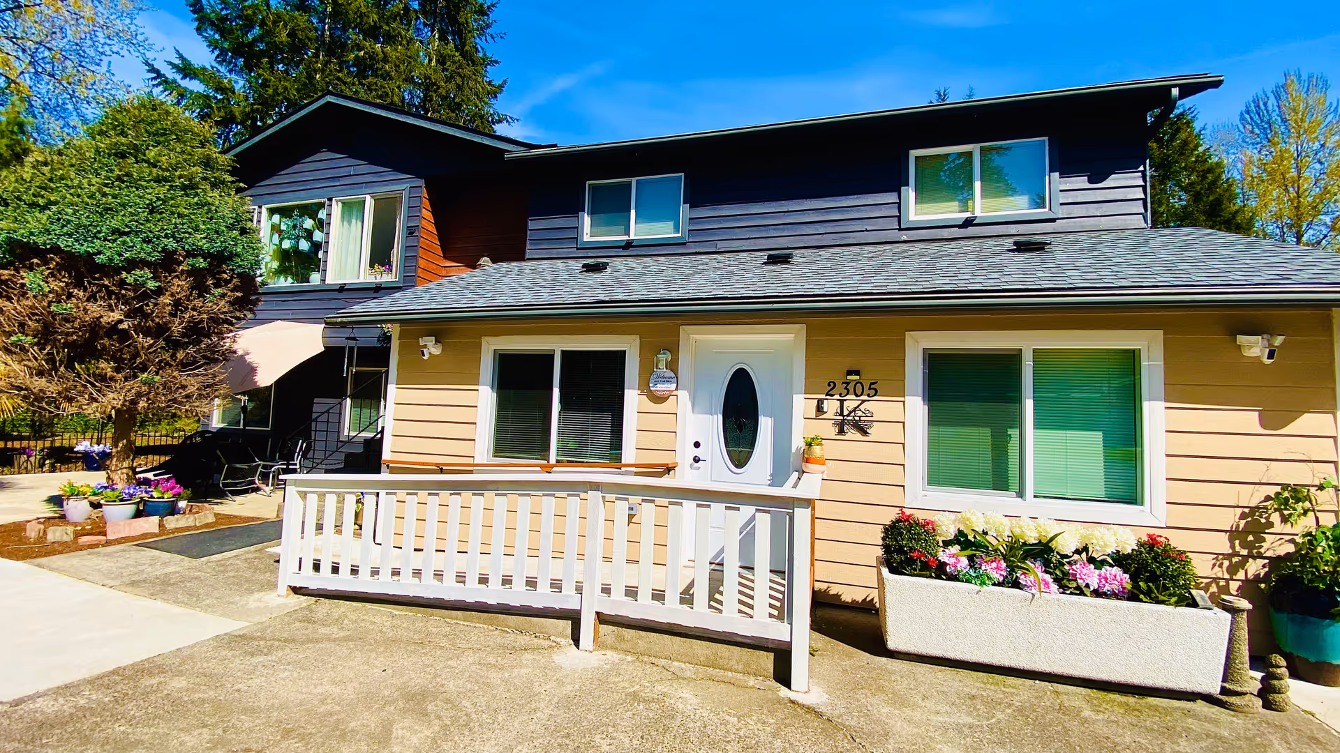 Two-story beige building with white railing, front door, and colorful planters.