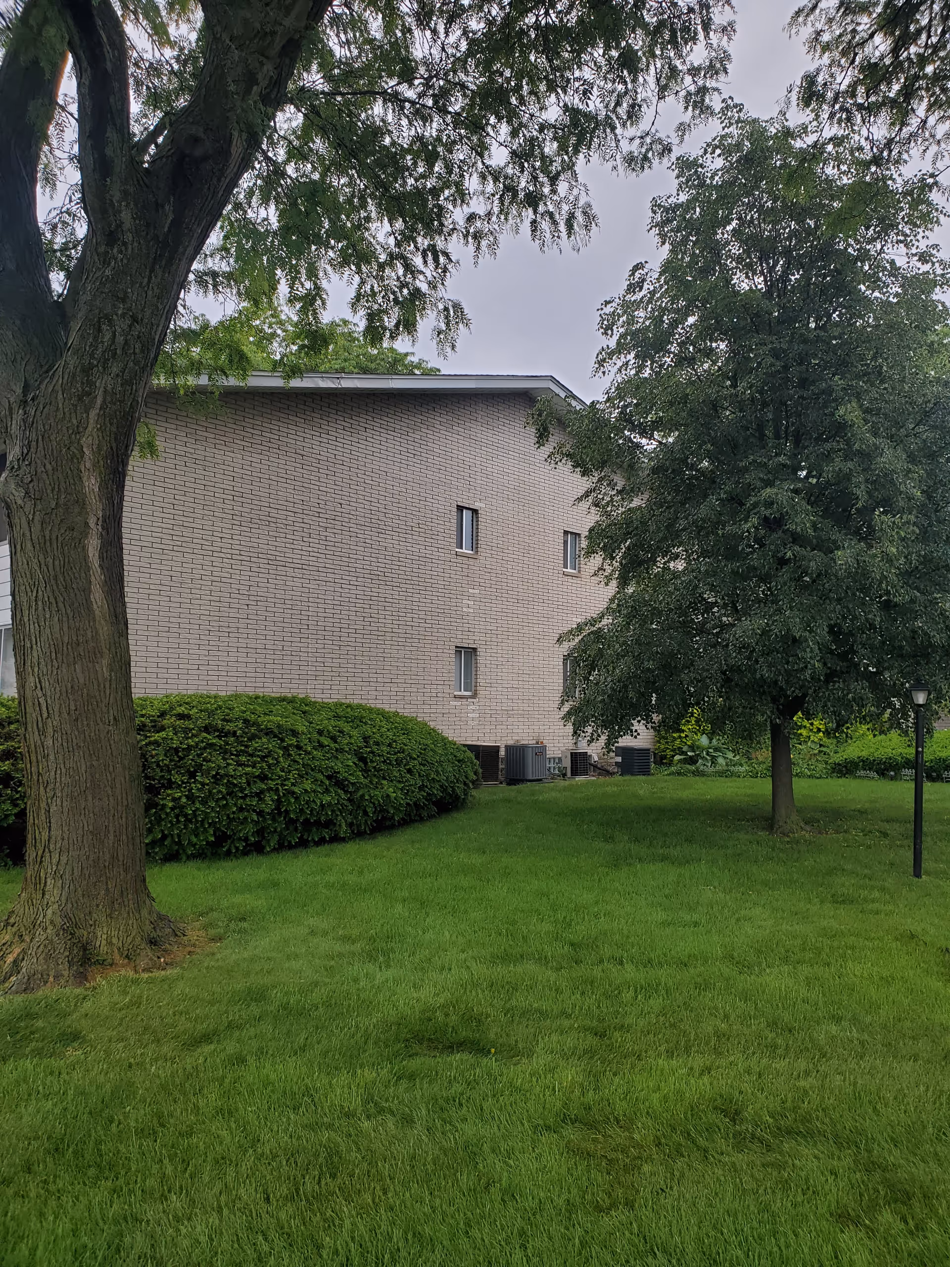 Exterior view of a brick senior living facility with green lawn and trees.