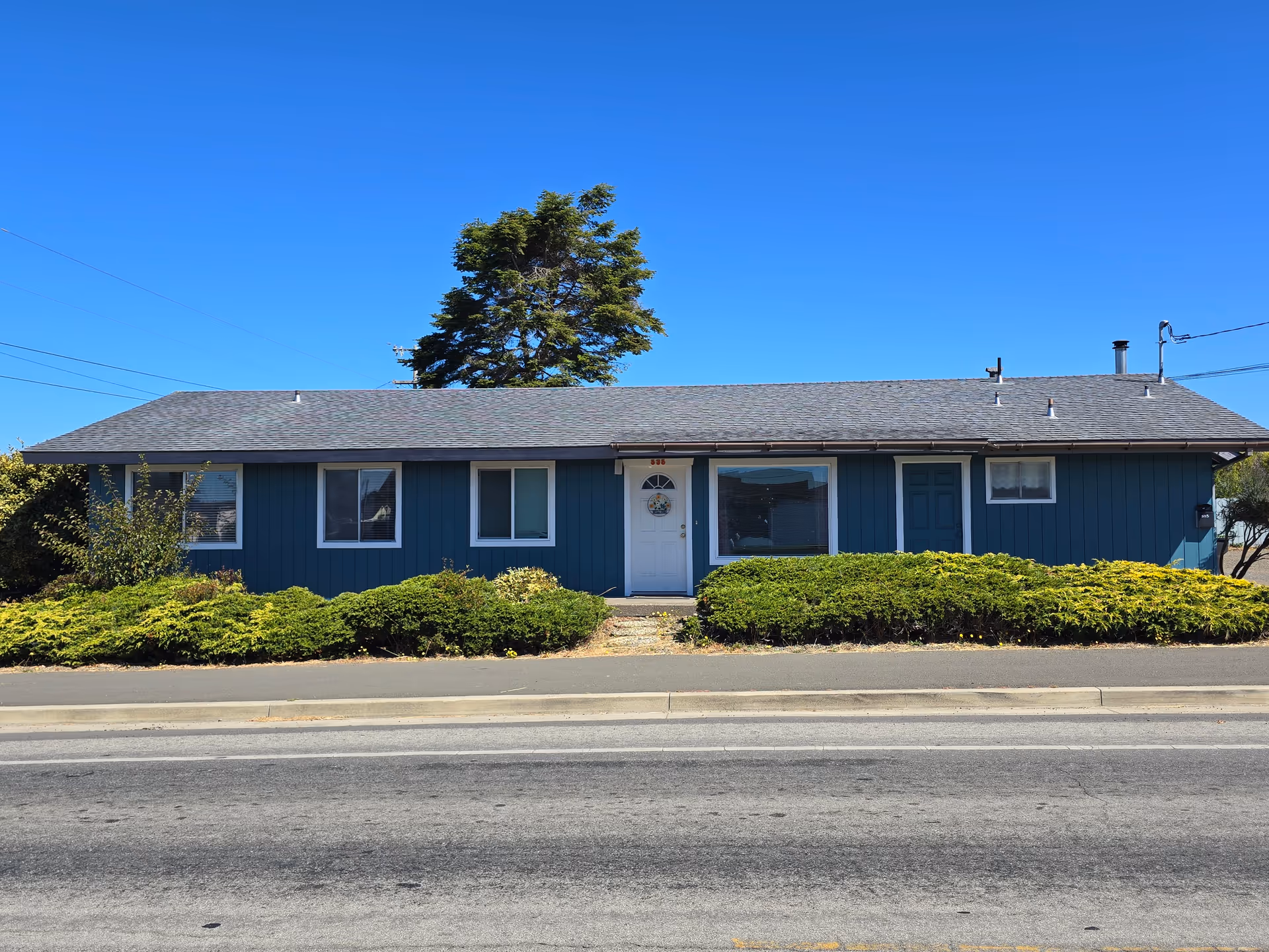 Blue single-story Oceanside Care Home exterior with shrubs along the front.