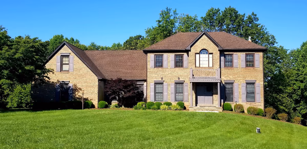 Brick two-story senior living facility with manicured lawn and surrounding trees.