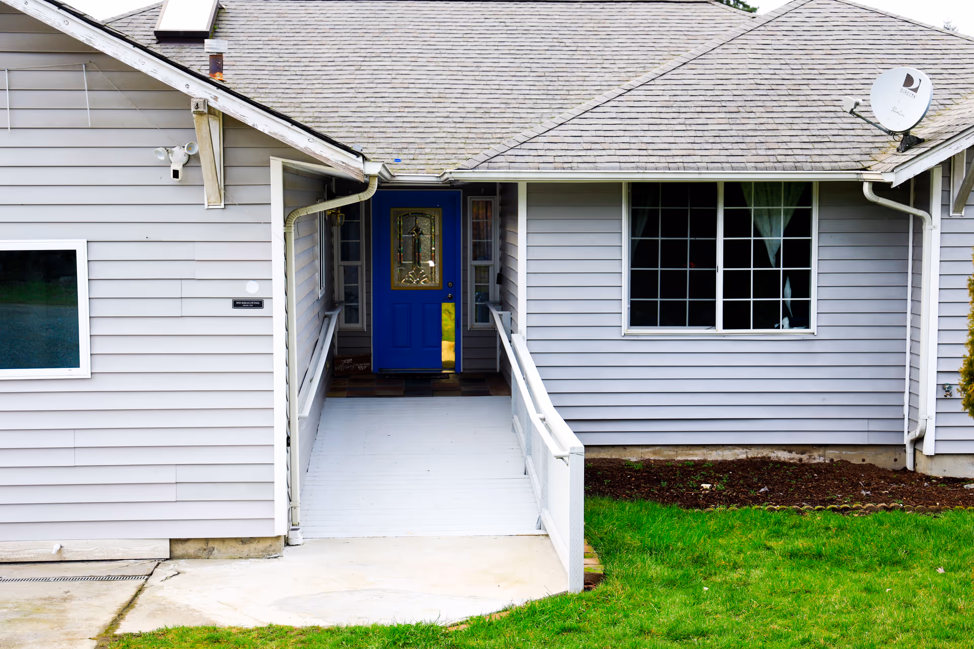 The building features grey siding, a blue front door, and a ramp.