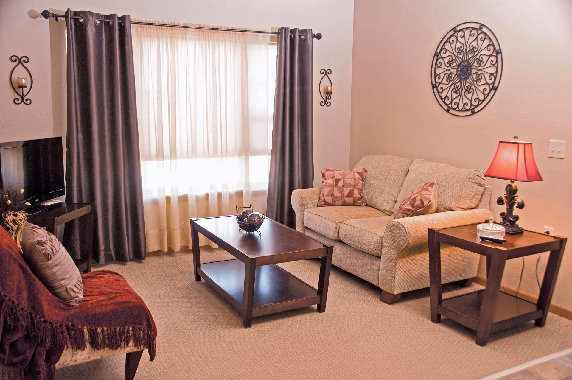 Cozy living room featuring beige sofa, dark coffee table, and window with sheer curtains.