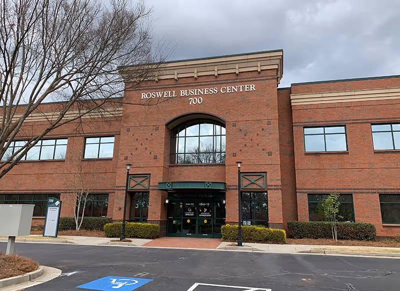 Brick business center with arched entrance labeled Roswell Business Center 700 and landscaping.