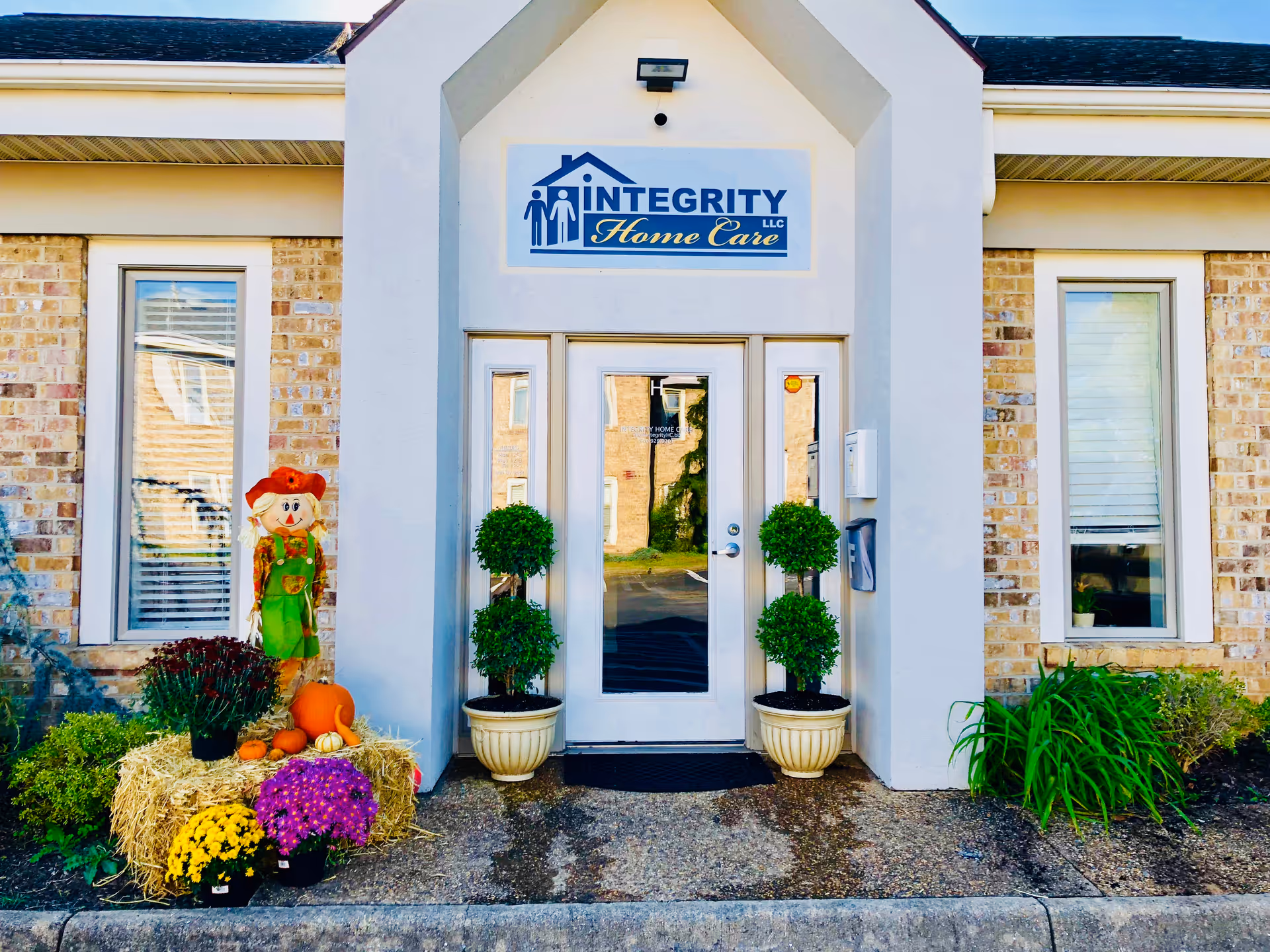Front entrance of Integrity Home Care LLC with two potted topiaries and autumn decor.