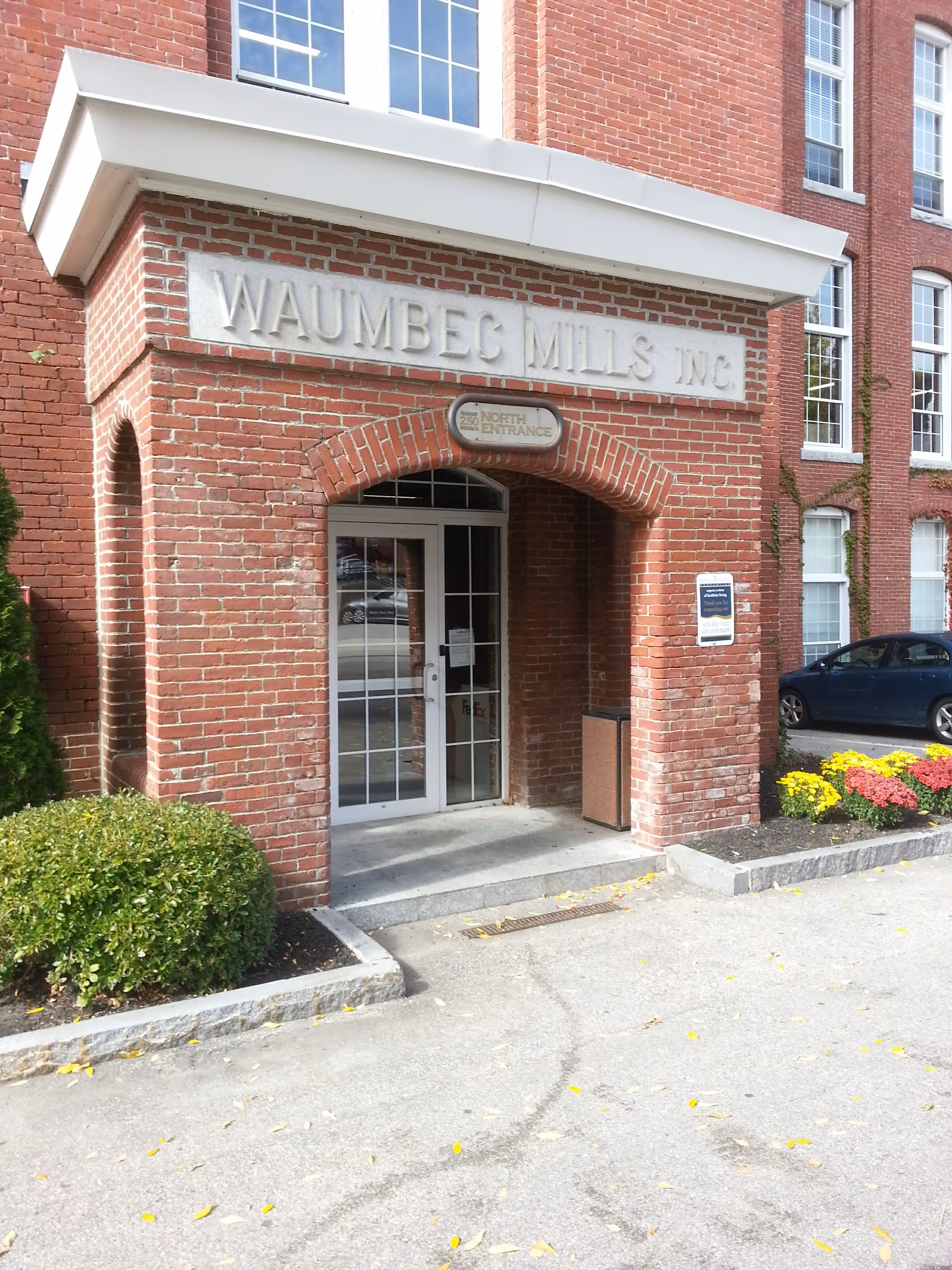 Brick building entrance with arched doorway and sign reading WAUMBEC MILLS INC above the doors
