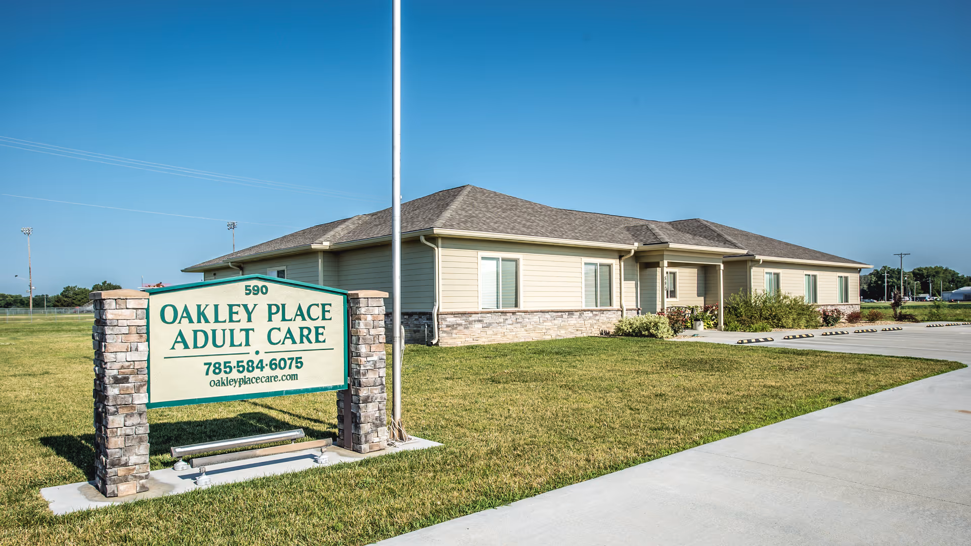 Front exterior of Oakley Place Adult Care building with a lawn, parking area, and a freestanding sign.