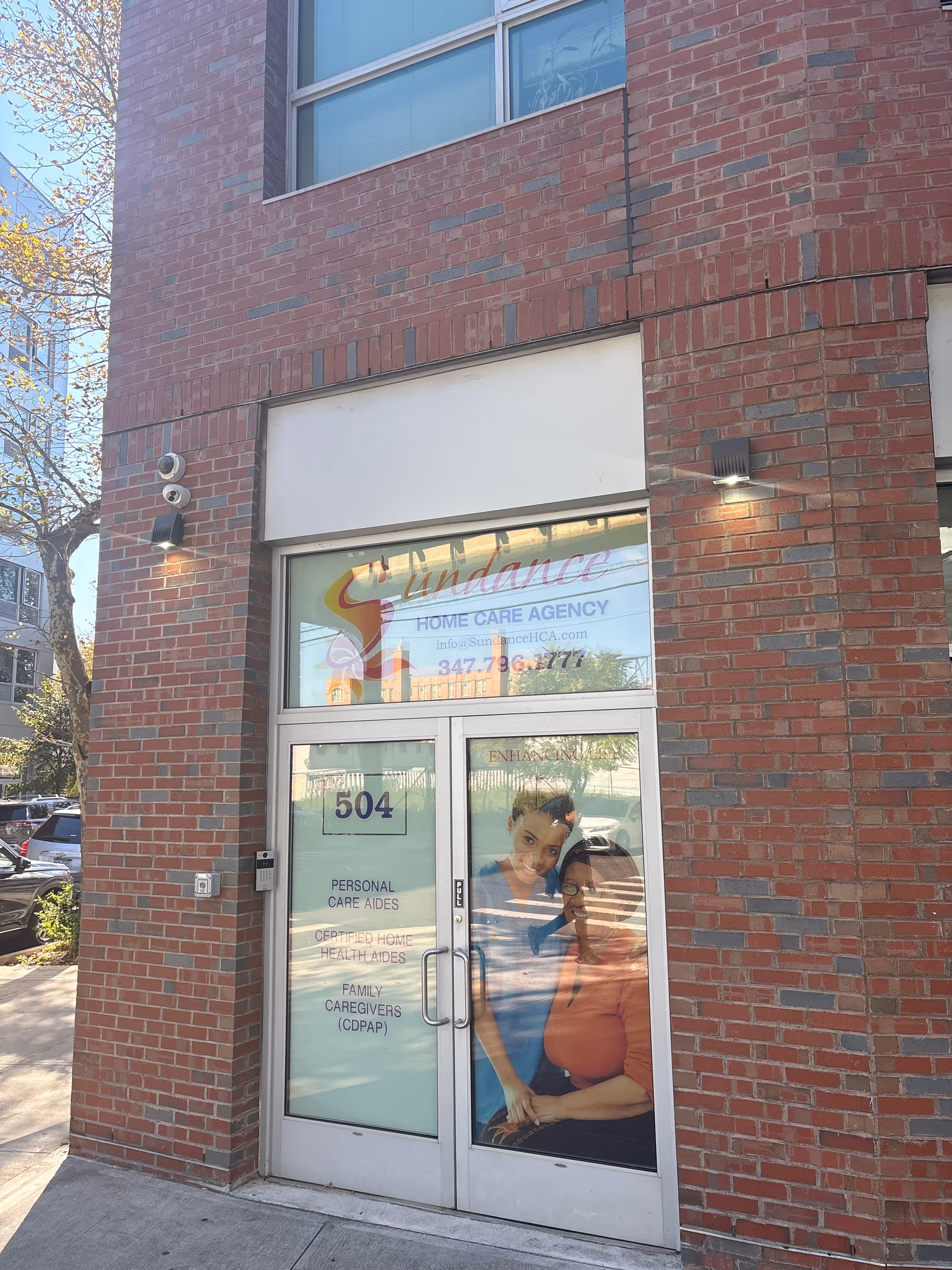 Brick building entrance with Sundance Home Care Agency sign and glass doors.