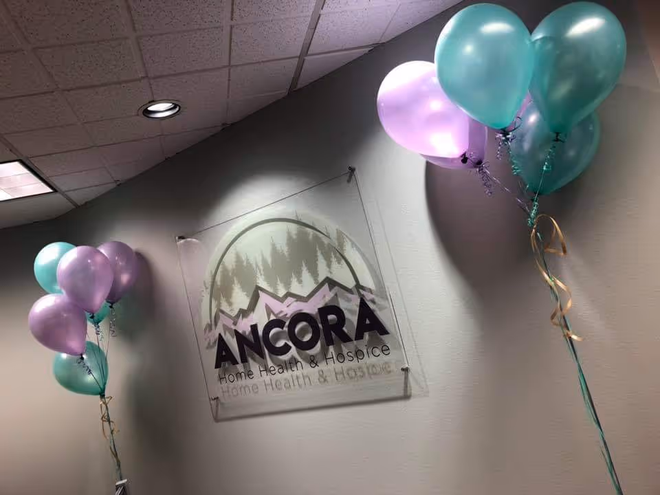 Interior lobby wall with ANCORA Home Health & Hospice sign and purple and teal balloons.