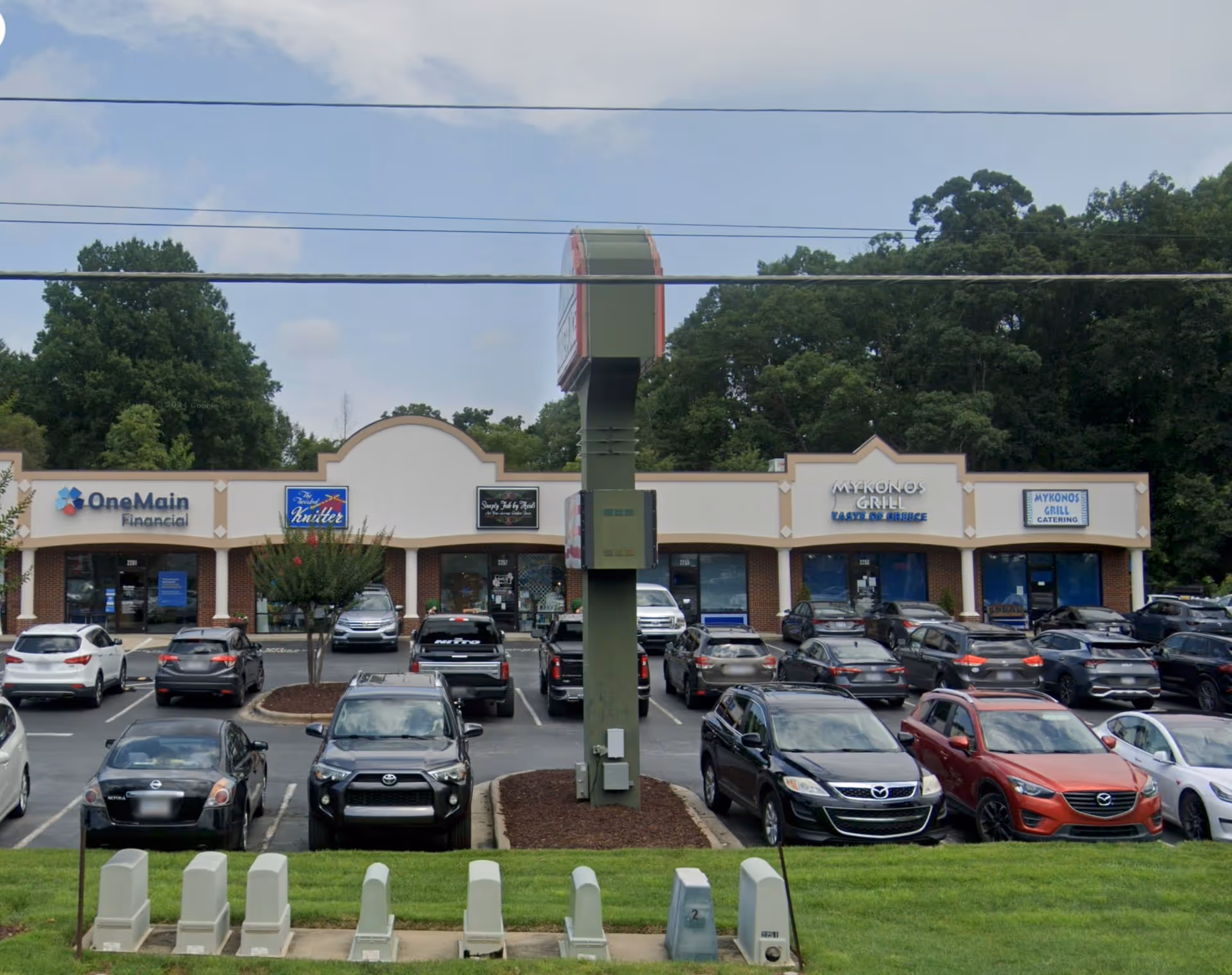 Parking lot in front of a shopping plaza with cars and a tall sign.