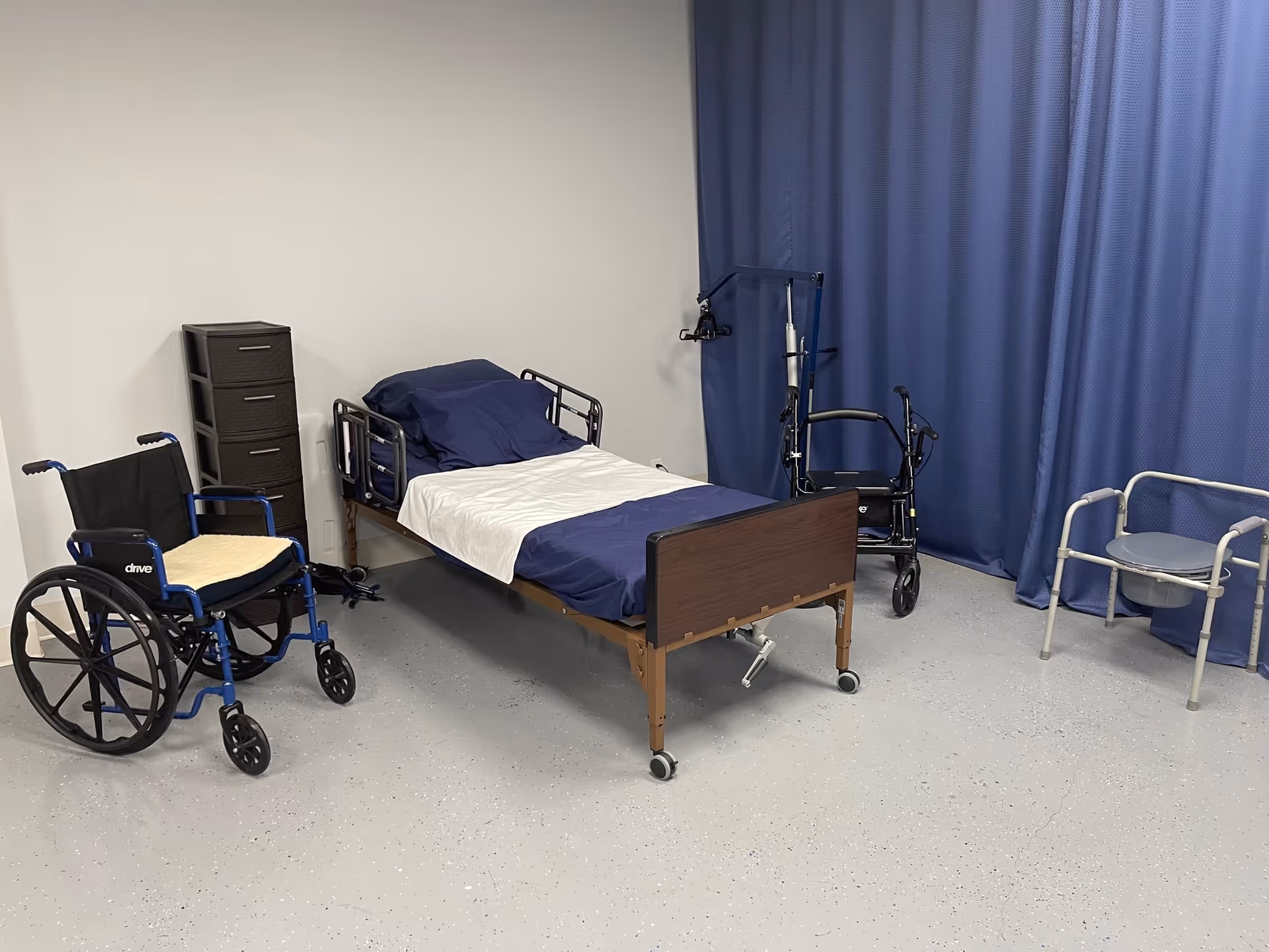 Hospital-style patient room with a bed, wheelchair, walker, and privacy blue curtain.
