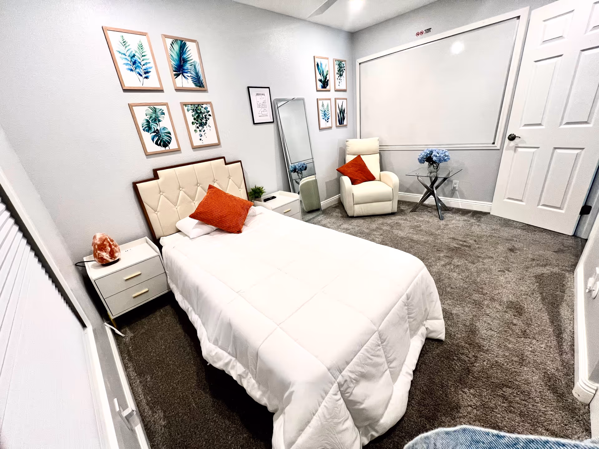 Small, neatly furnished bedroom with a bed, white furniture, wall art, and a seating area.