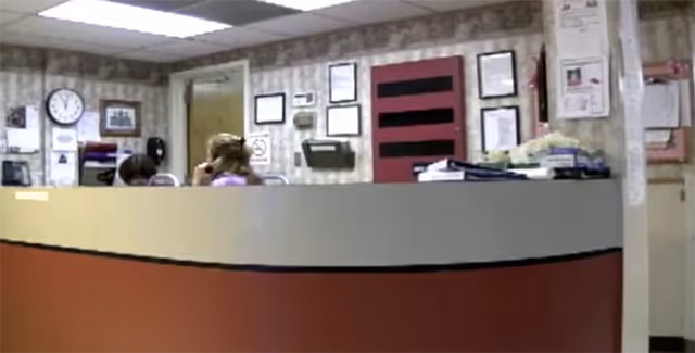 Reception desk in a patterned lobby with wall decor, clock, and paperwork.