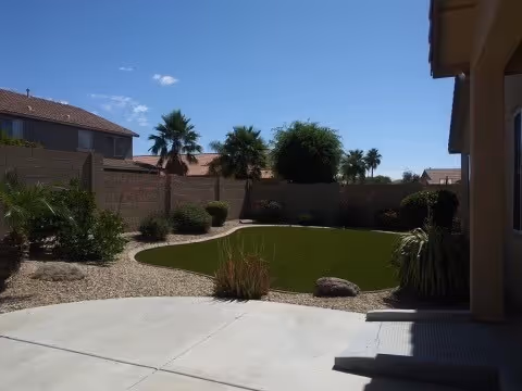 Sunny backyard courtyard of Love and Care I Assisted Living with lawn, palm trees, and walls.
