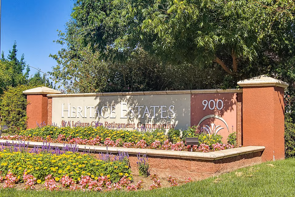 Entrance sign for Heritage Estates with blooming flower beds and greenery.