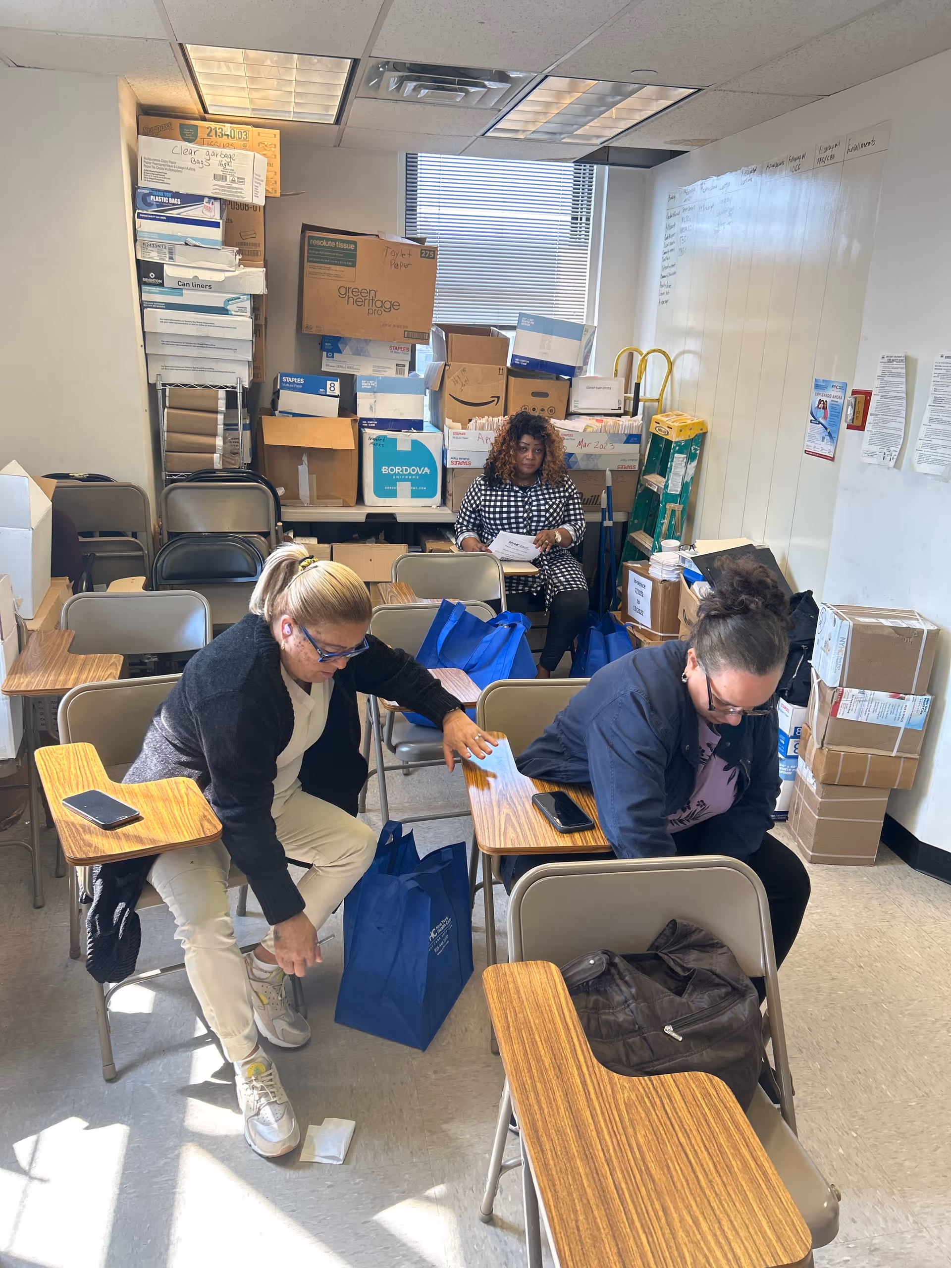 Cluttered supply room with three staff sorting boxes at New York Health Care, Inc.