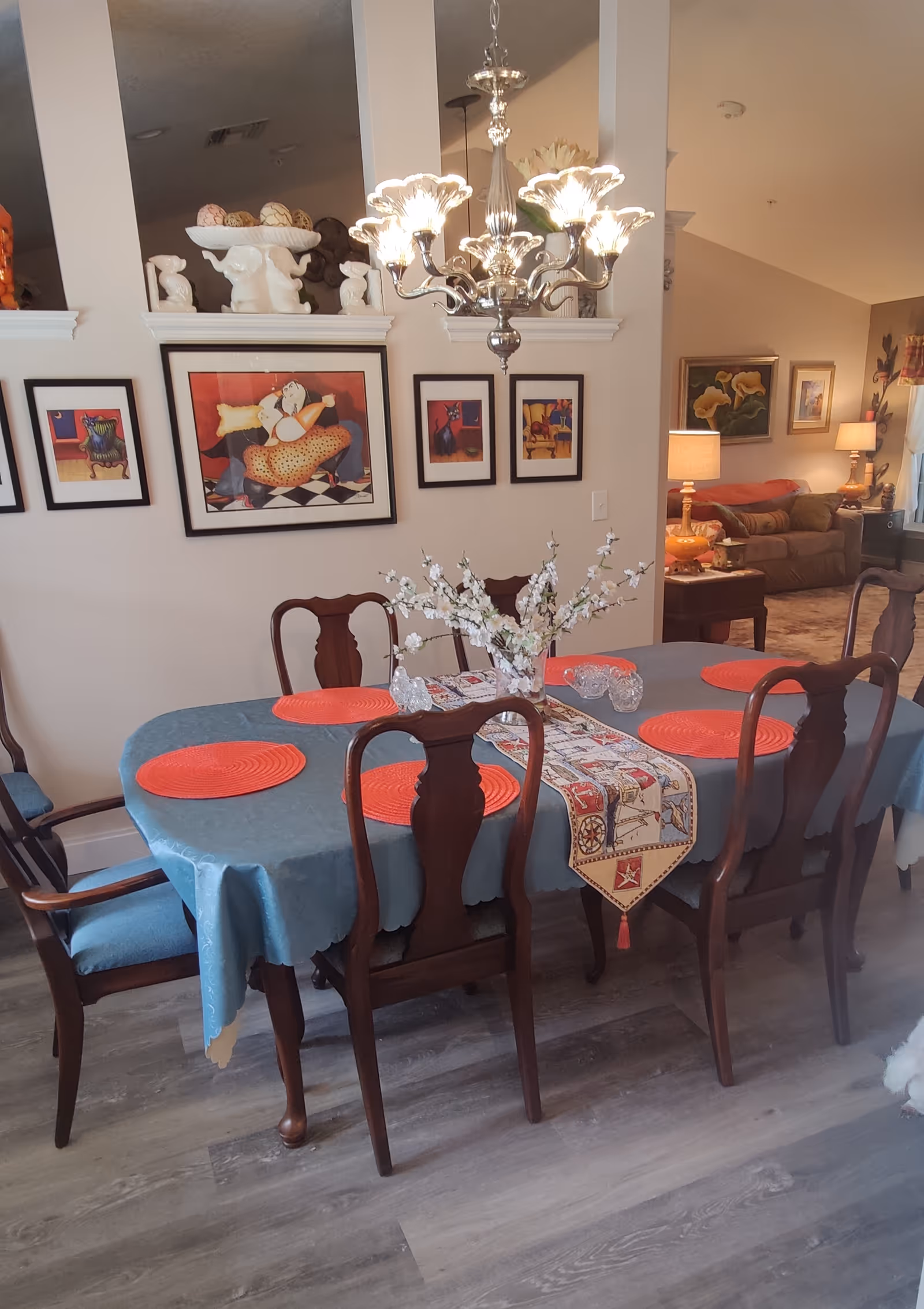 A dining room with a table set for six, framed art, and a chandelier.
