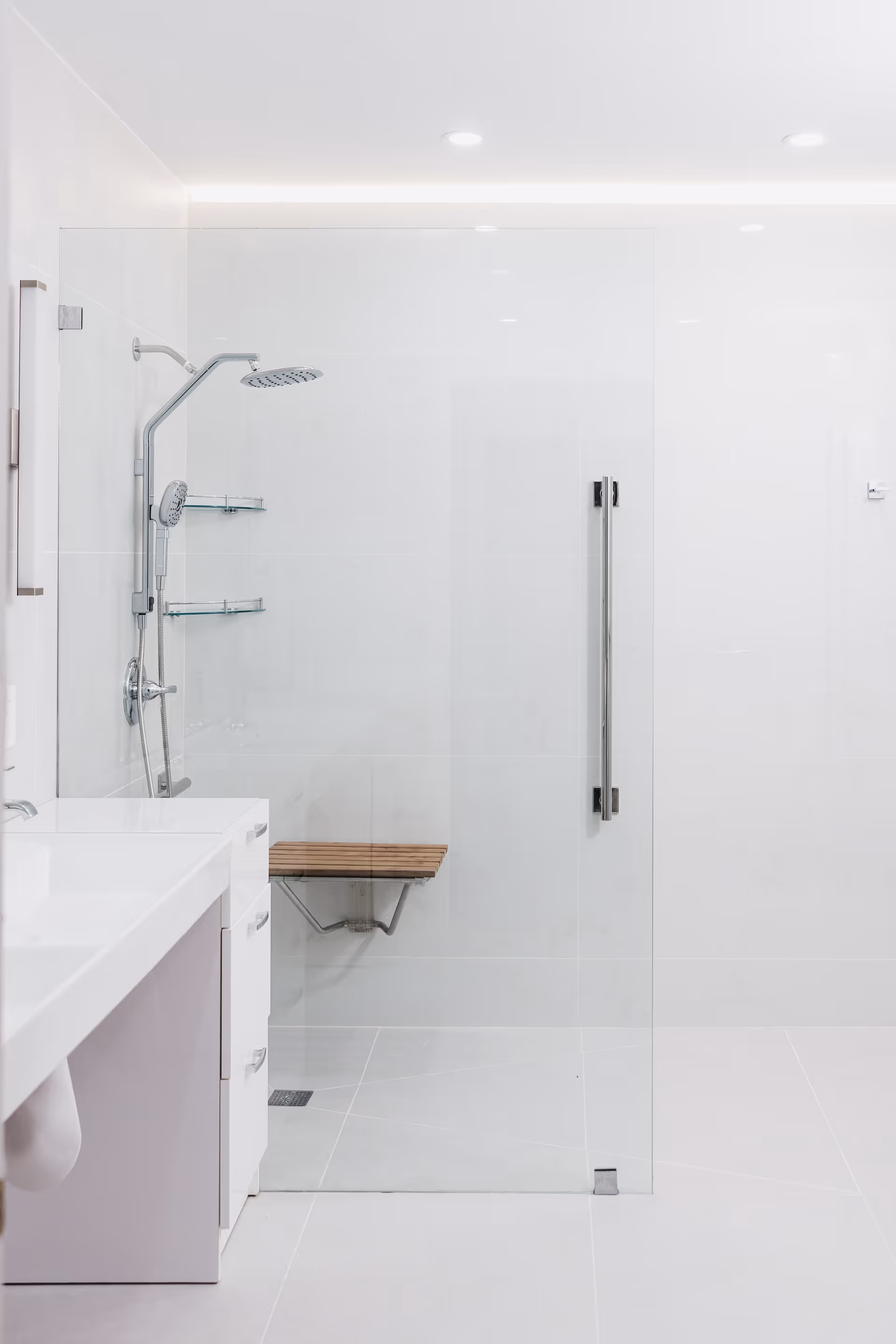 Modern white bathroom with glass shower enclosure, bench, and sink.