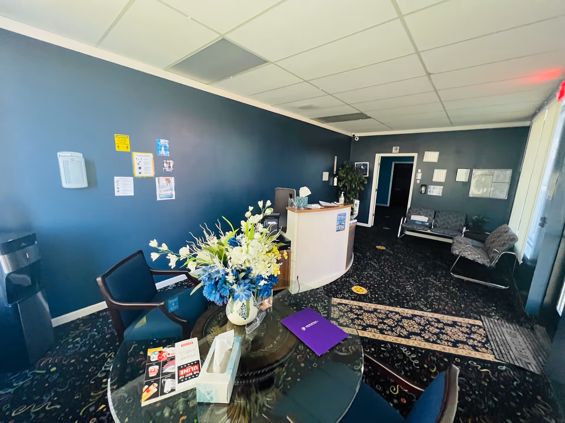 Reception area of a blue-walled senior living lobby with a glass round table and flowers.