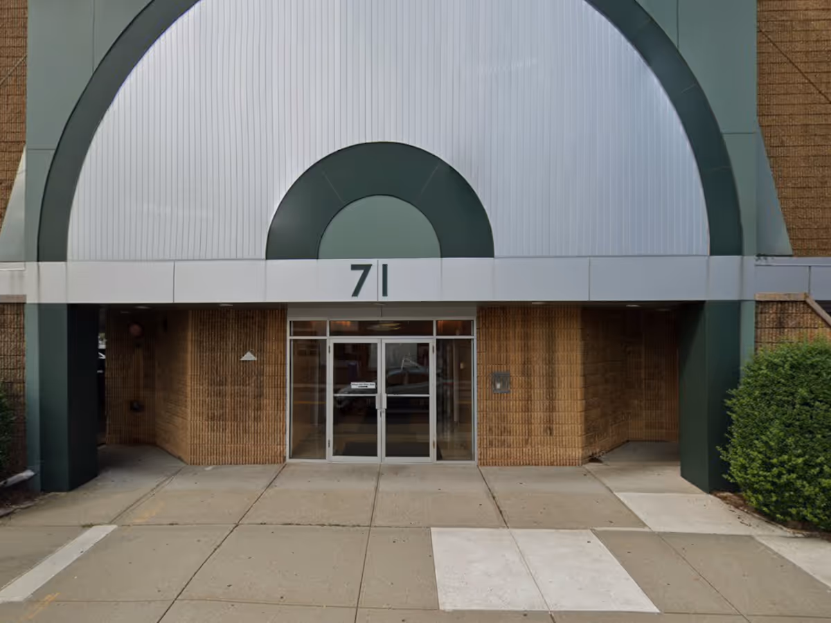Front entrance of a brick building with a curved metal canopy and 71 sign.