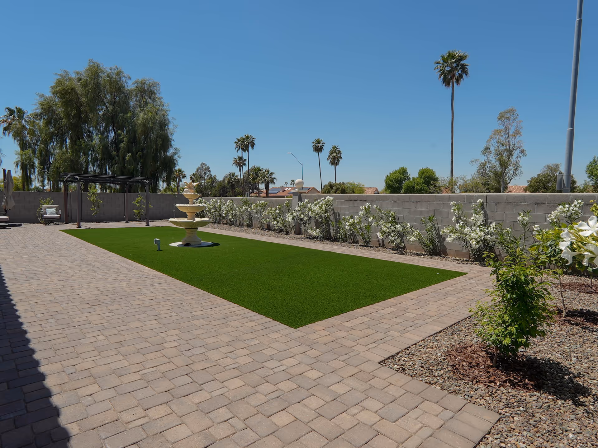 Sunny outdoor courtyard with a central fountain, brick paving, and palms.