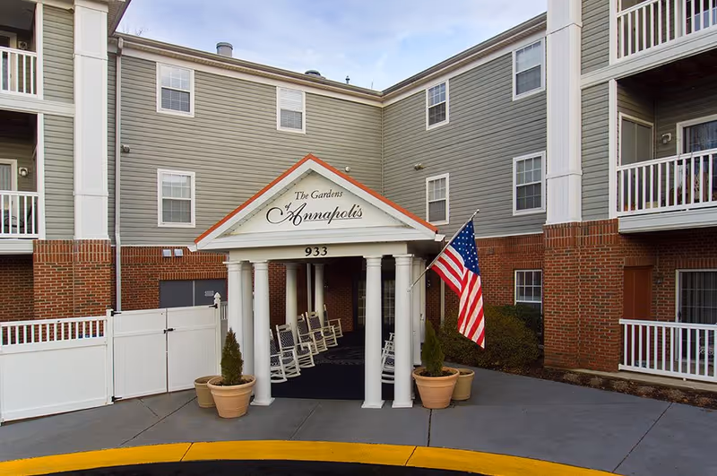 Front entrance of The Gardens Annapolis senior living with columns and American flag.