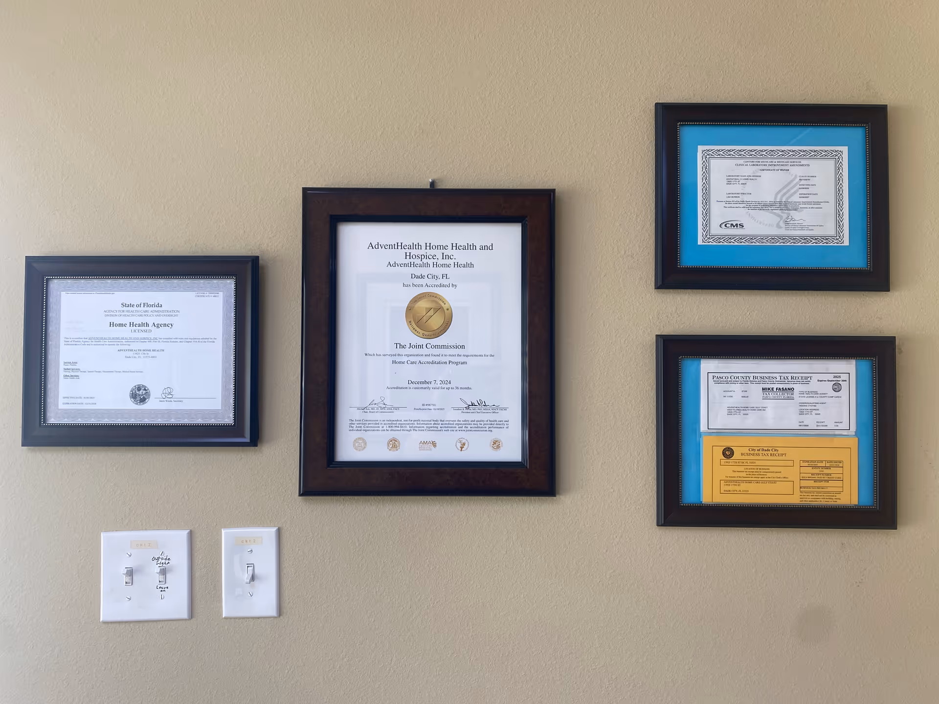 Beige wall with four framed certificates and two light switches beneath.