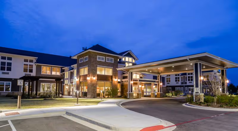 Exterior view of Ignite Medical Resort Fort Worth at dusk, showing a modern two-story building with large windows and a covered entrance driveway, illuminated by outdoor lights.
